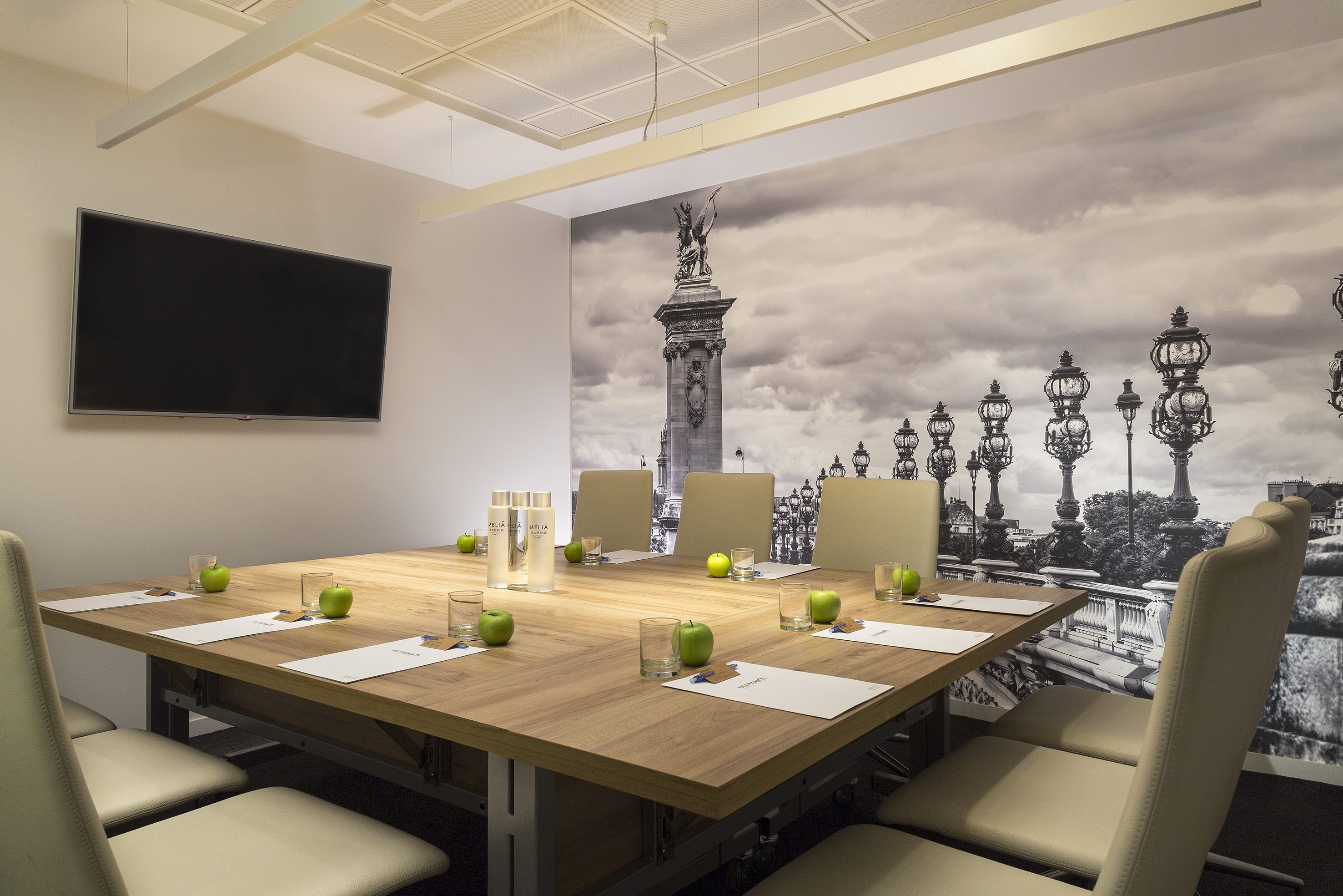 Modern meeting room with large wooden table, TV, and iconic Paris cityscape mural.
