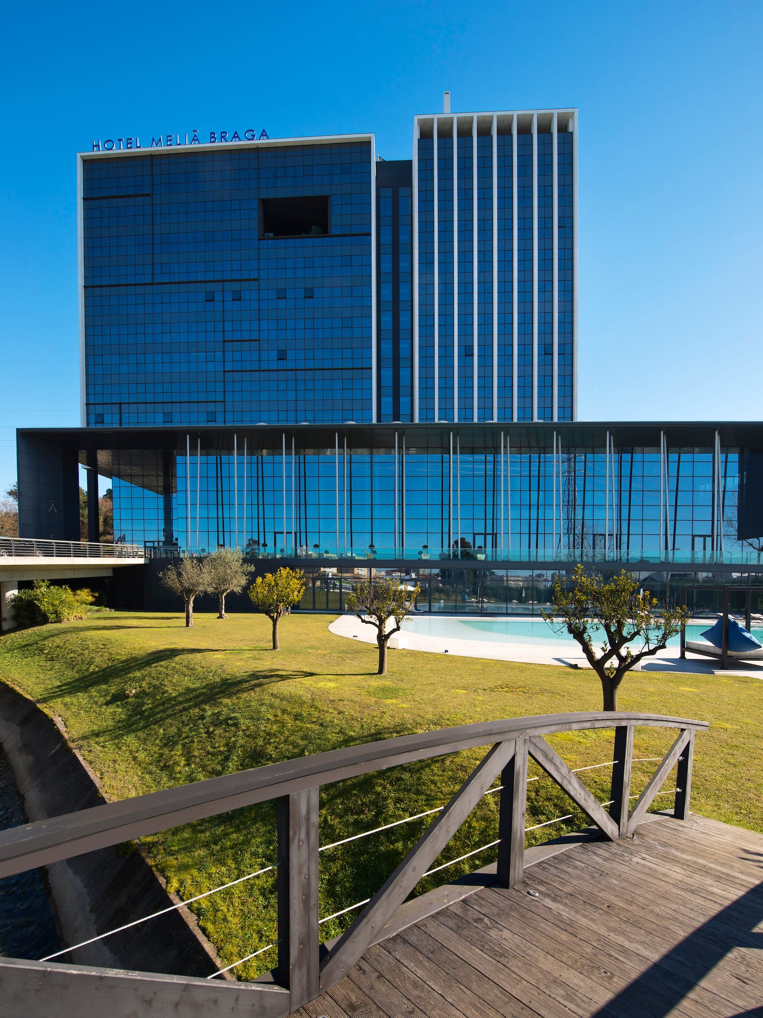 a bridge over a grass lawn with trees and a building in the background