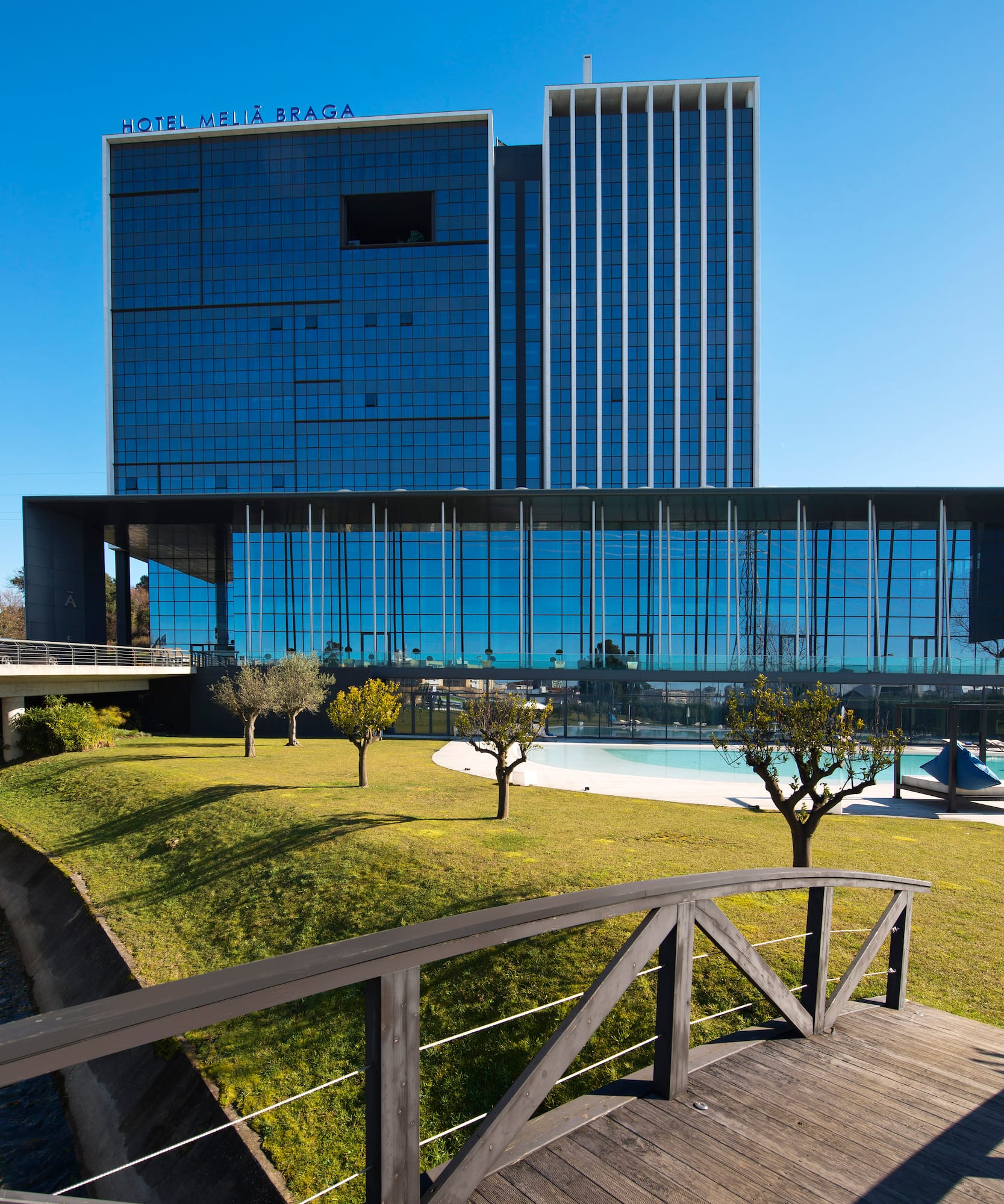 a bridge over a grass lawn with trees and a building in the background