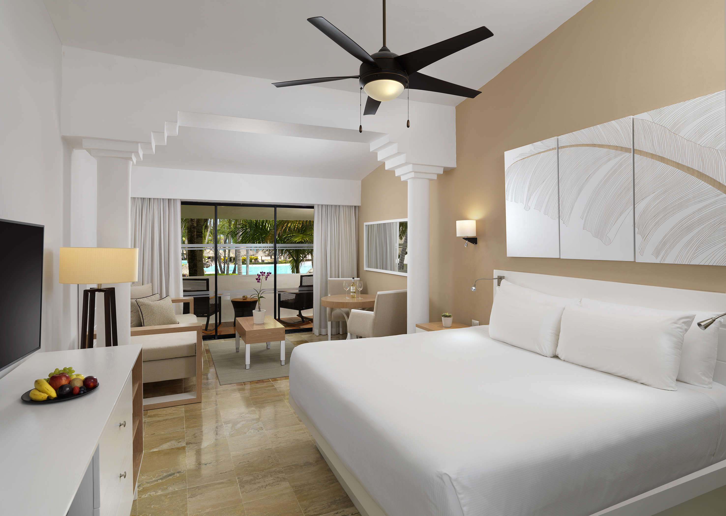 Hotel suite with king bed, living area, and tropical pool view.