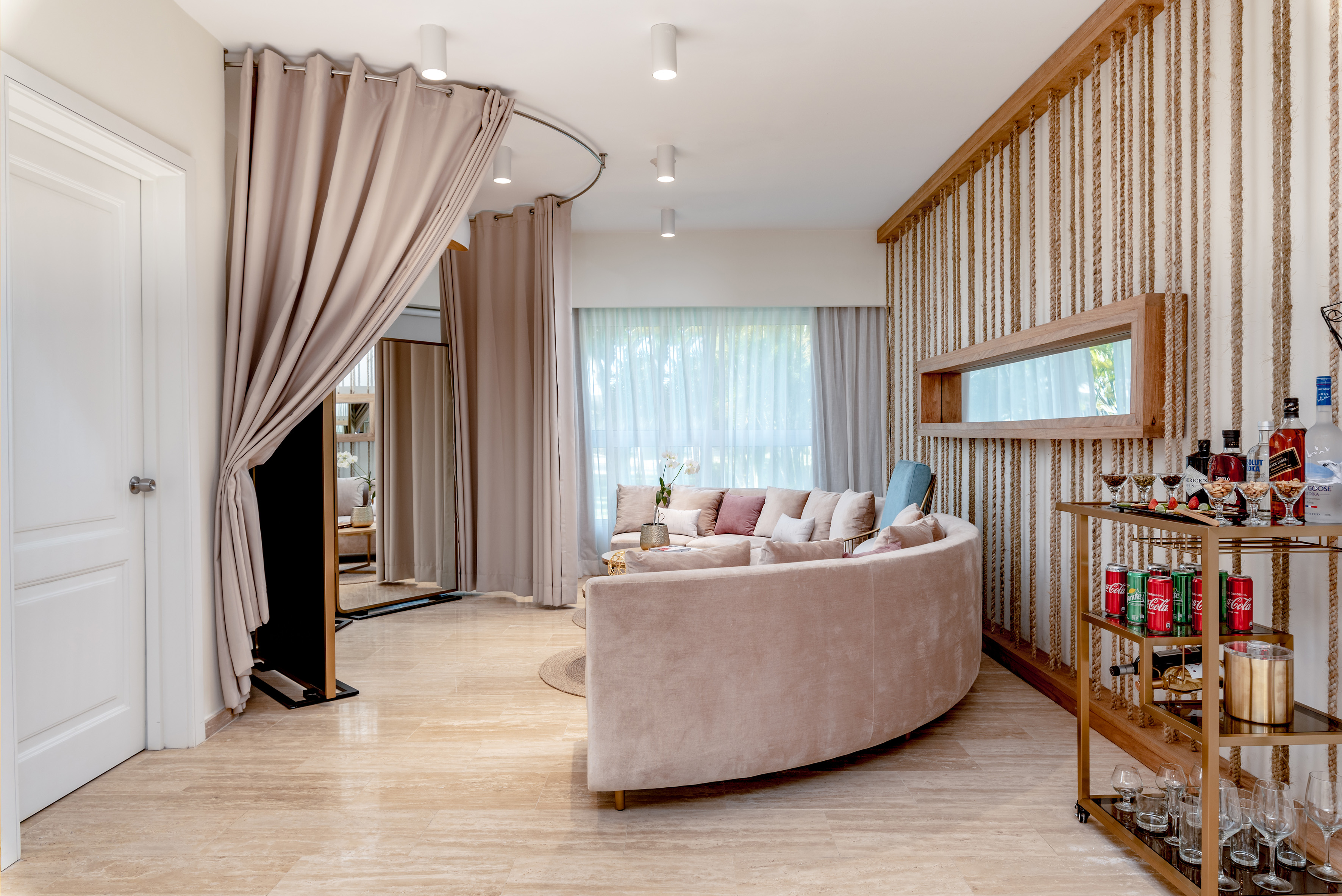 Lounge area with curved pink velvet sofa, bar cart, and unique rope wall.