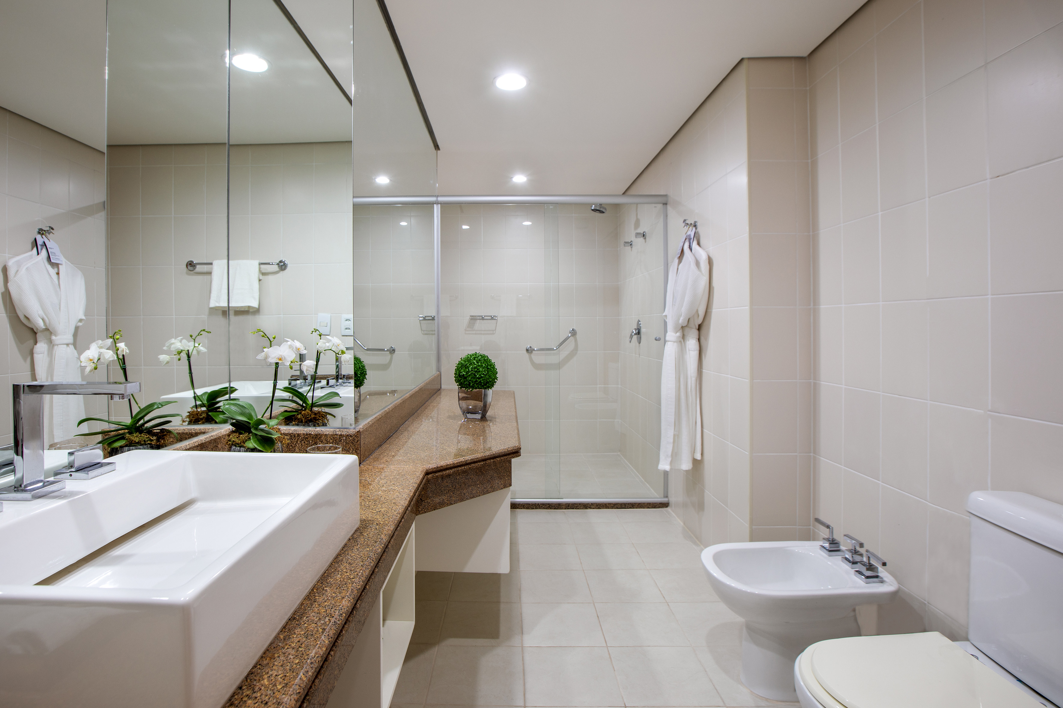 Clean modern bathroom with vanity, glass shower, toilet, and white orchids.