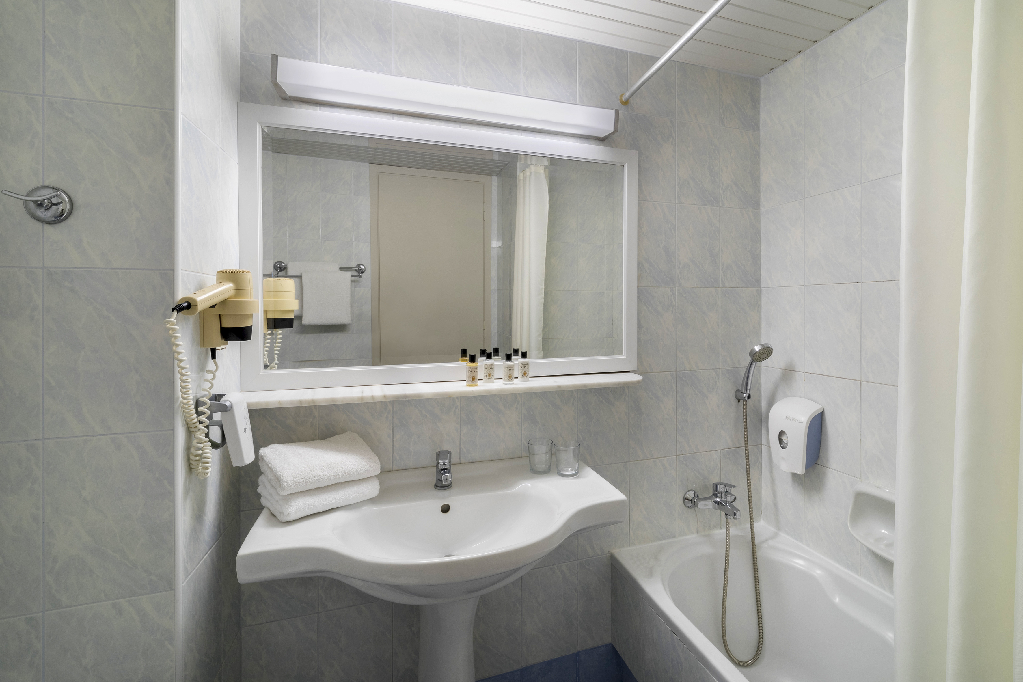 Tiled hotel guest bathroom with sink, mirror, bathtub, shower, and hairdryer.