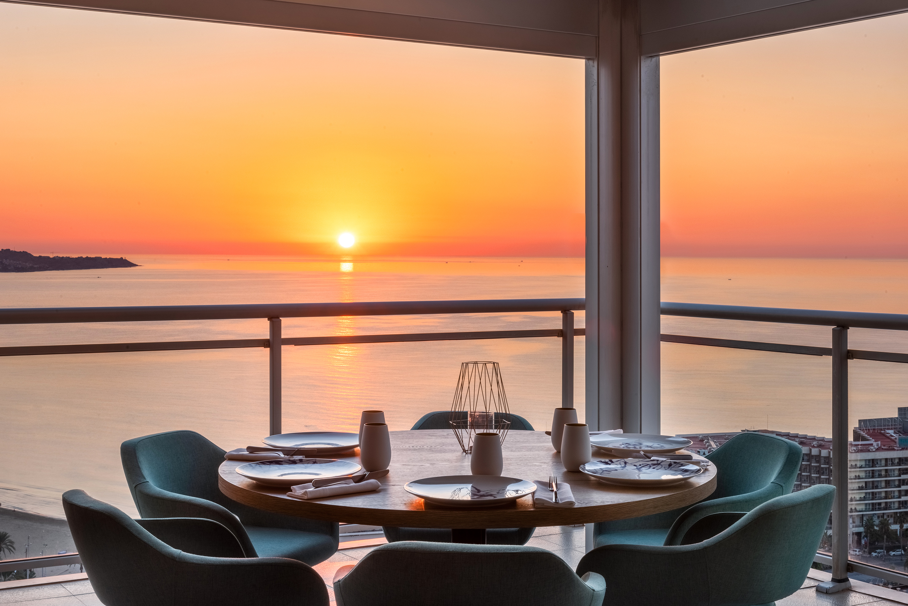 Balcony restaurant dining table set overlooking a vibrant ocean sunset.