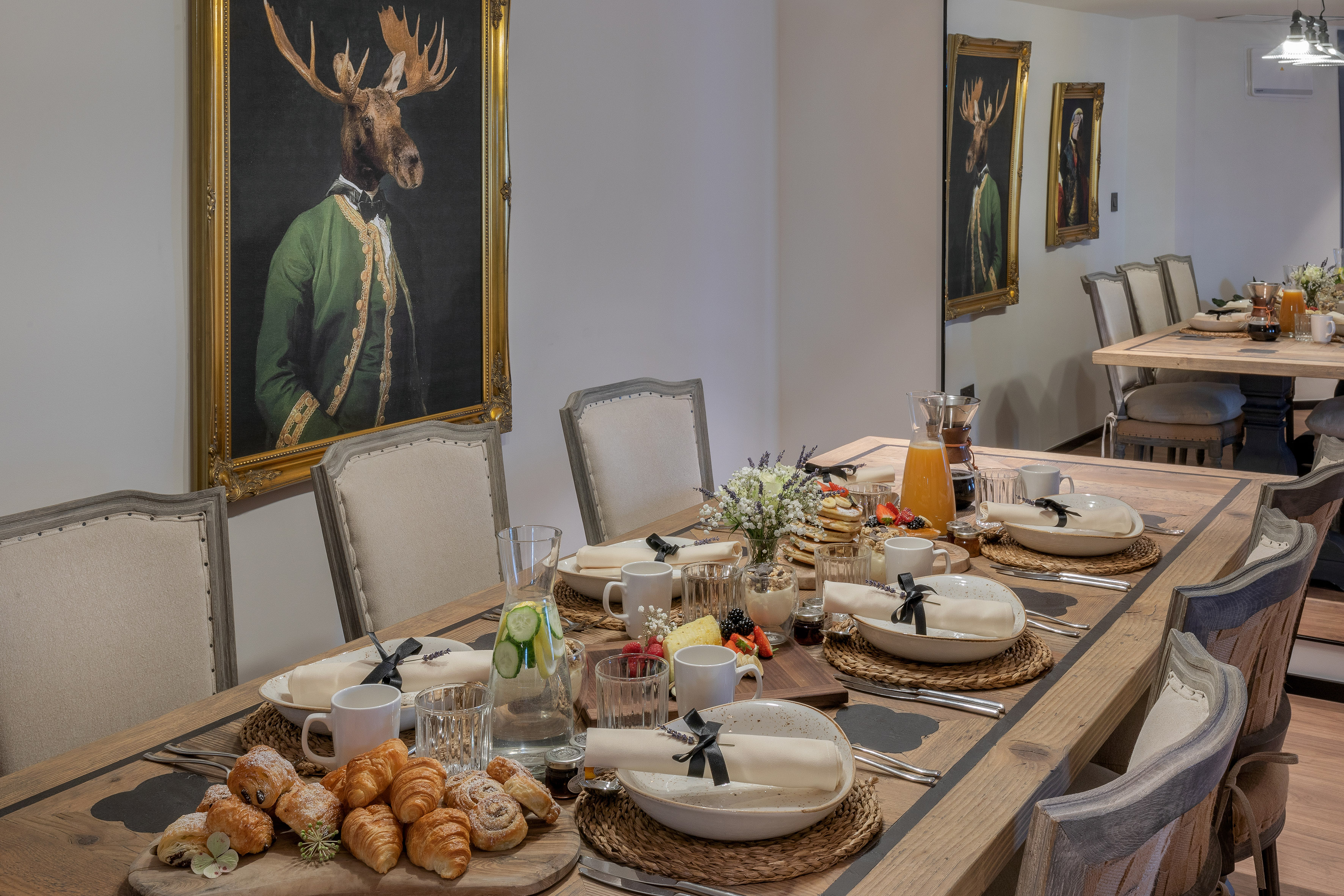 Rustic dining table set with pastries, fruit, and a framed moose portrait.