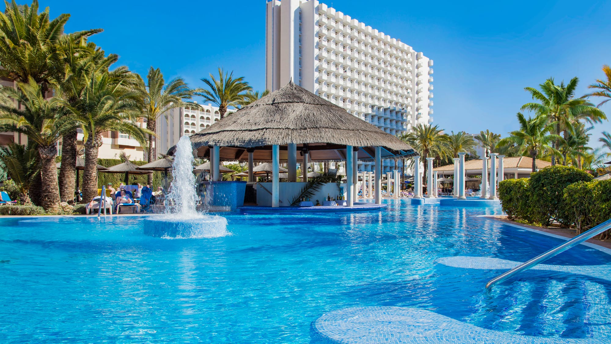 a pool with water fountain and a thatched roof