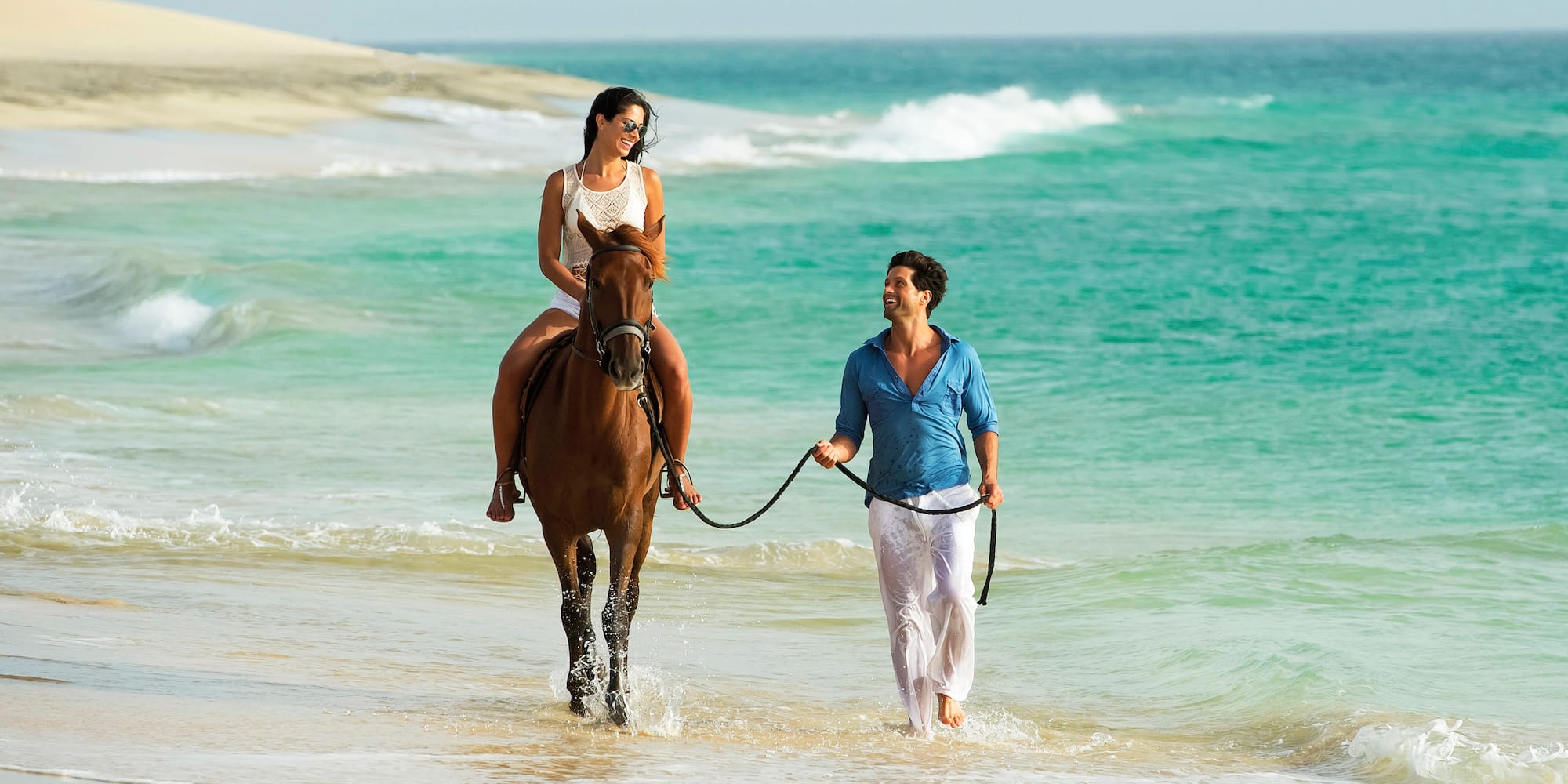 a man and woman on a horse on a beach