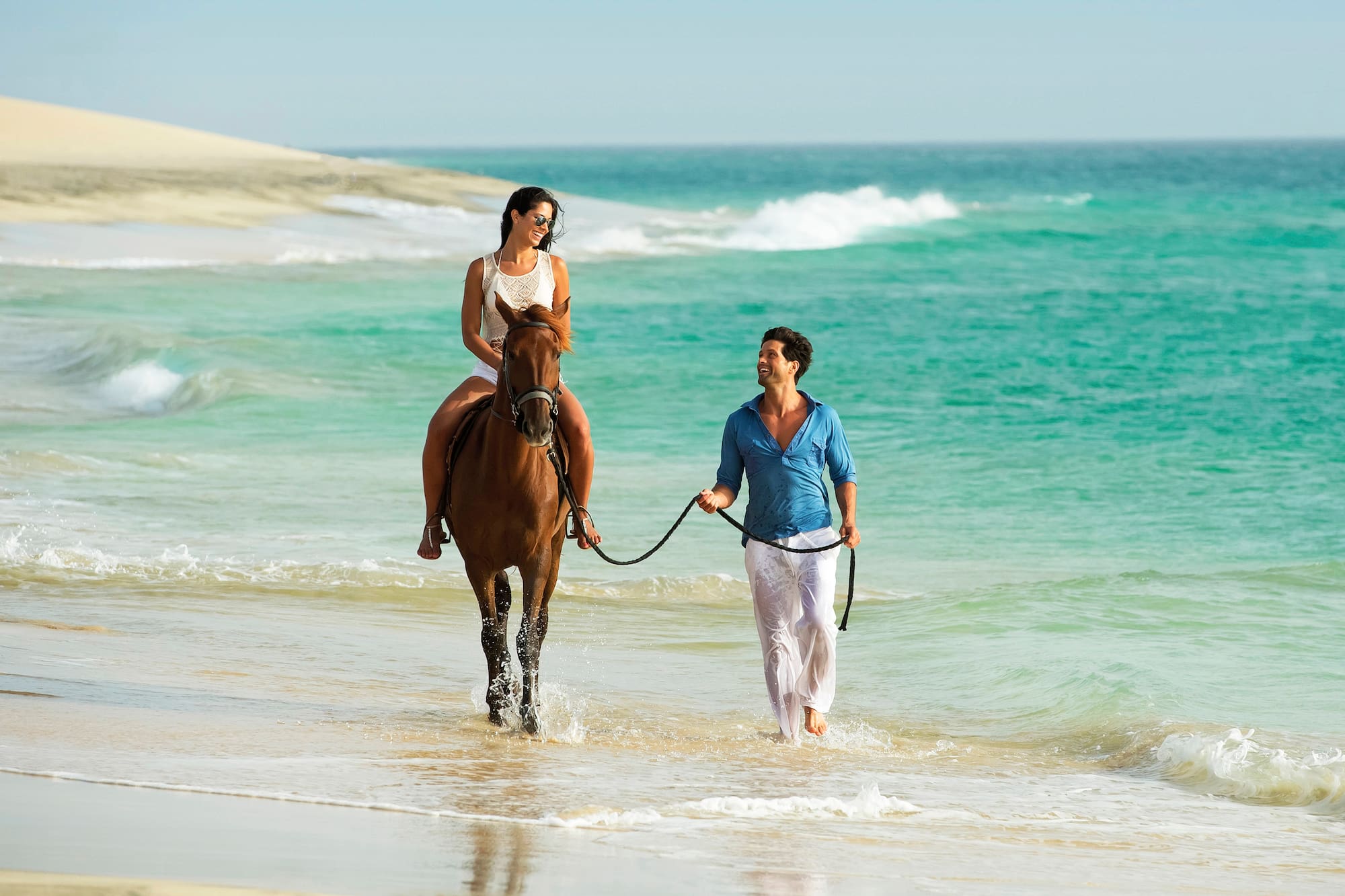 Happy couple horseback riding on a tropical beach with turquoise water.