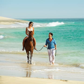 a man and woman on a horse on a beach
