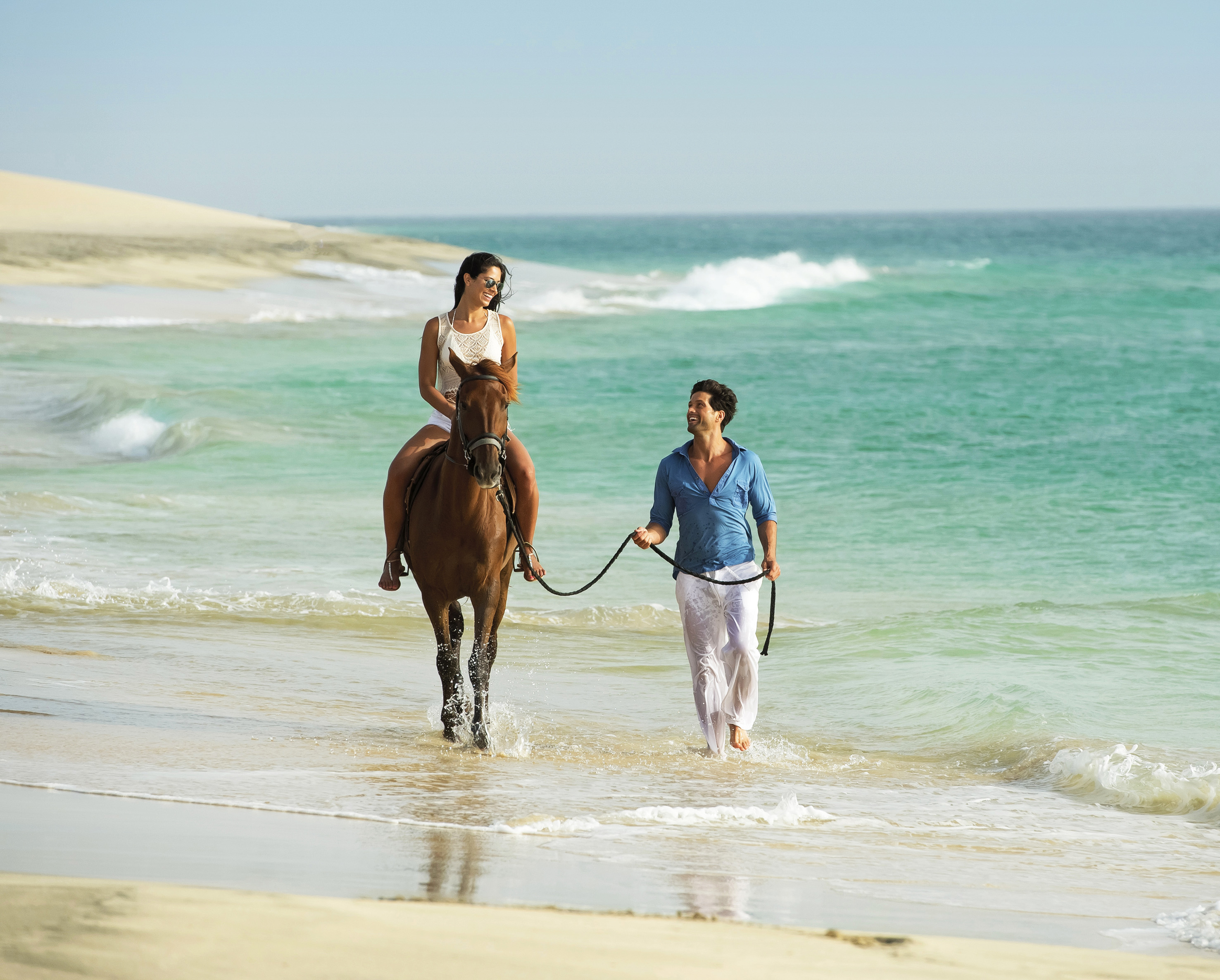 Happy couple horseback riding on a tropical beach with turquoise water.