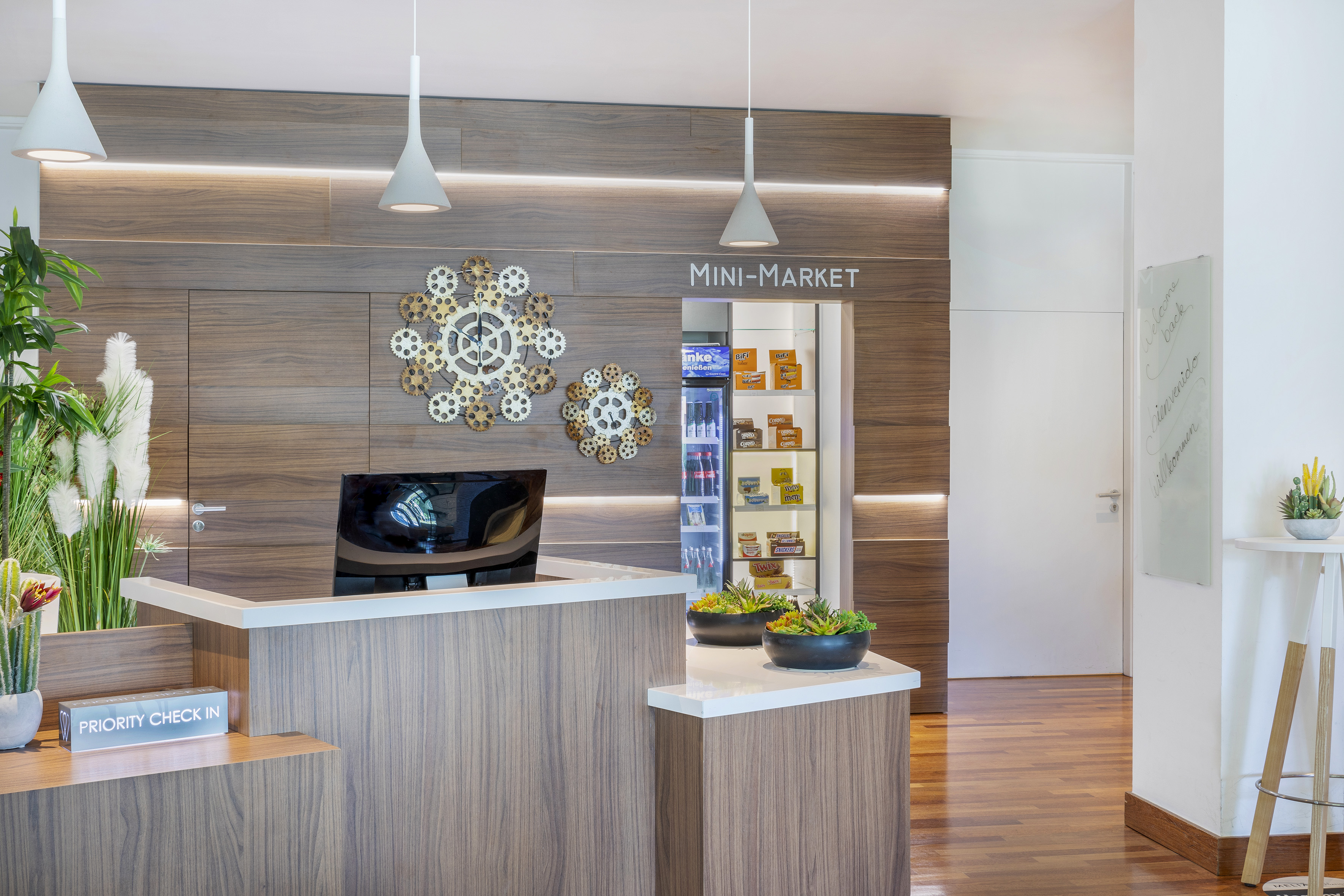 Modern hotel reception desk with a mini-market and "Priority Check In" sign.