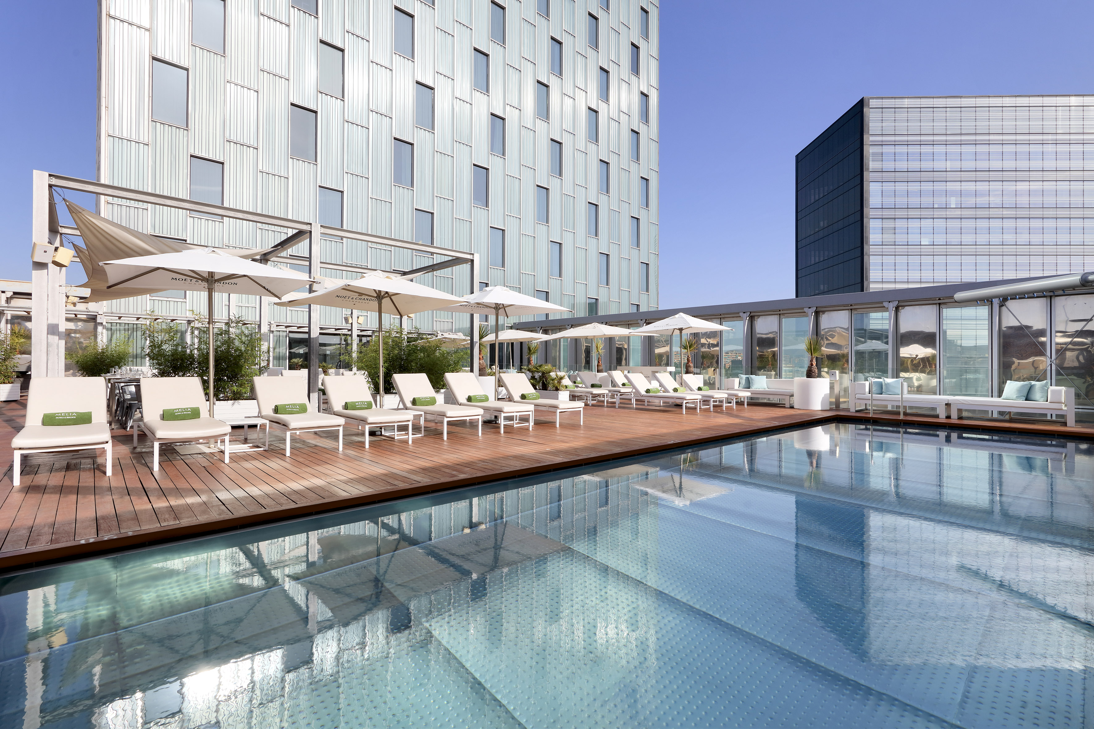 Rooftop hotel pool with lounge chairs, umbrellas, and modern building.