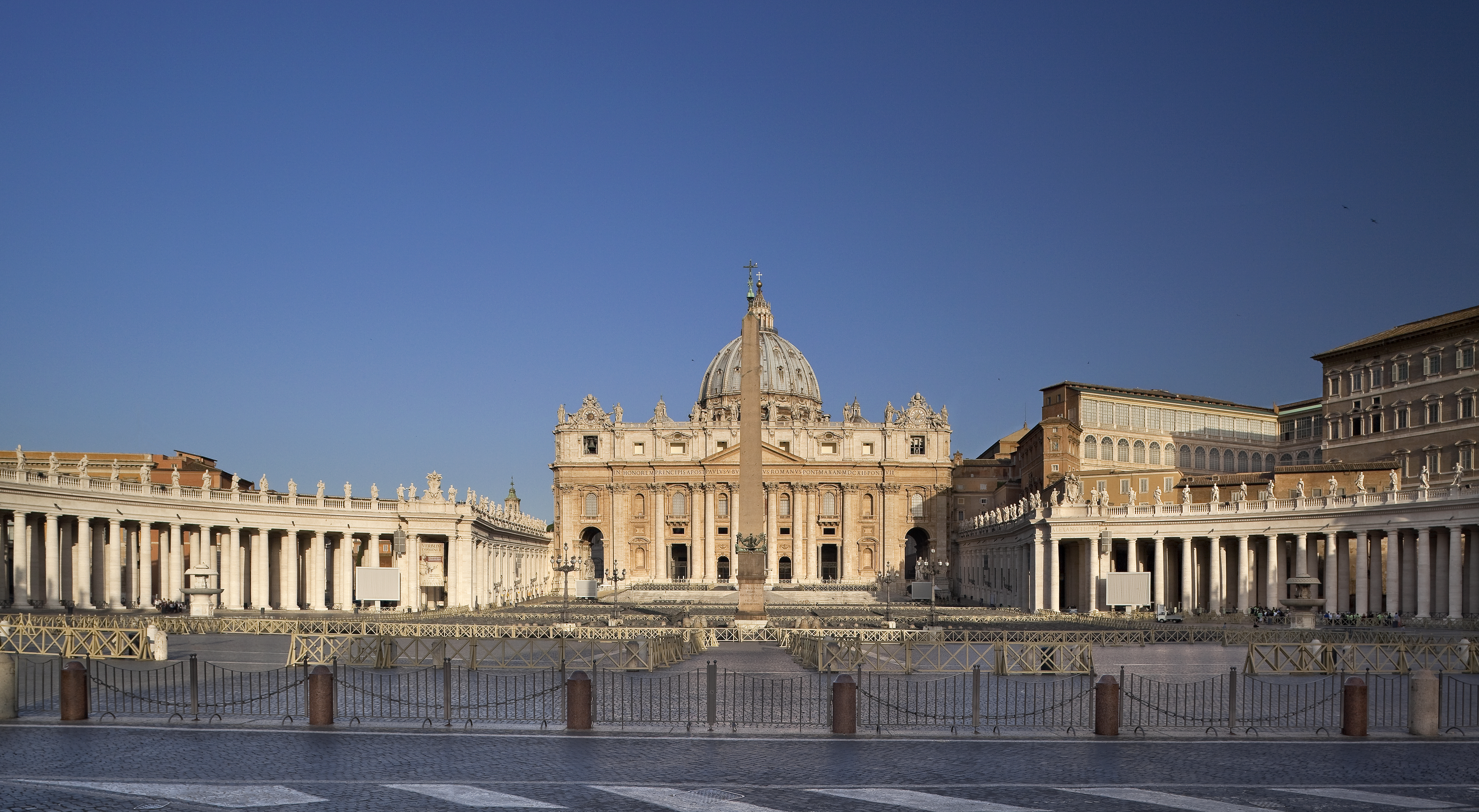 St. Peter's Basilica, Vatican Square, obelisk, and colonnades under clear sky.