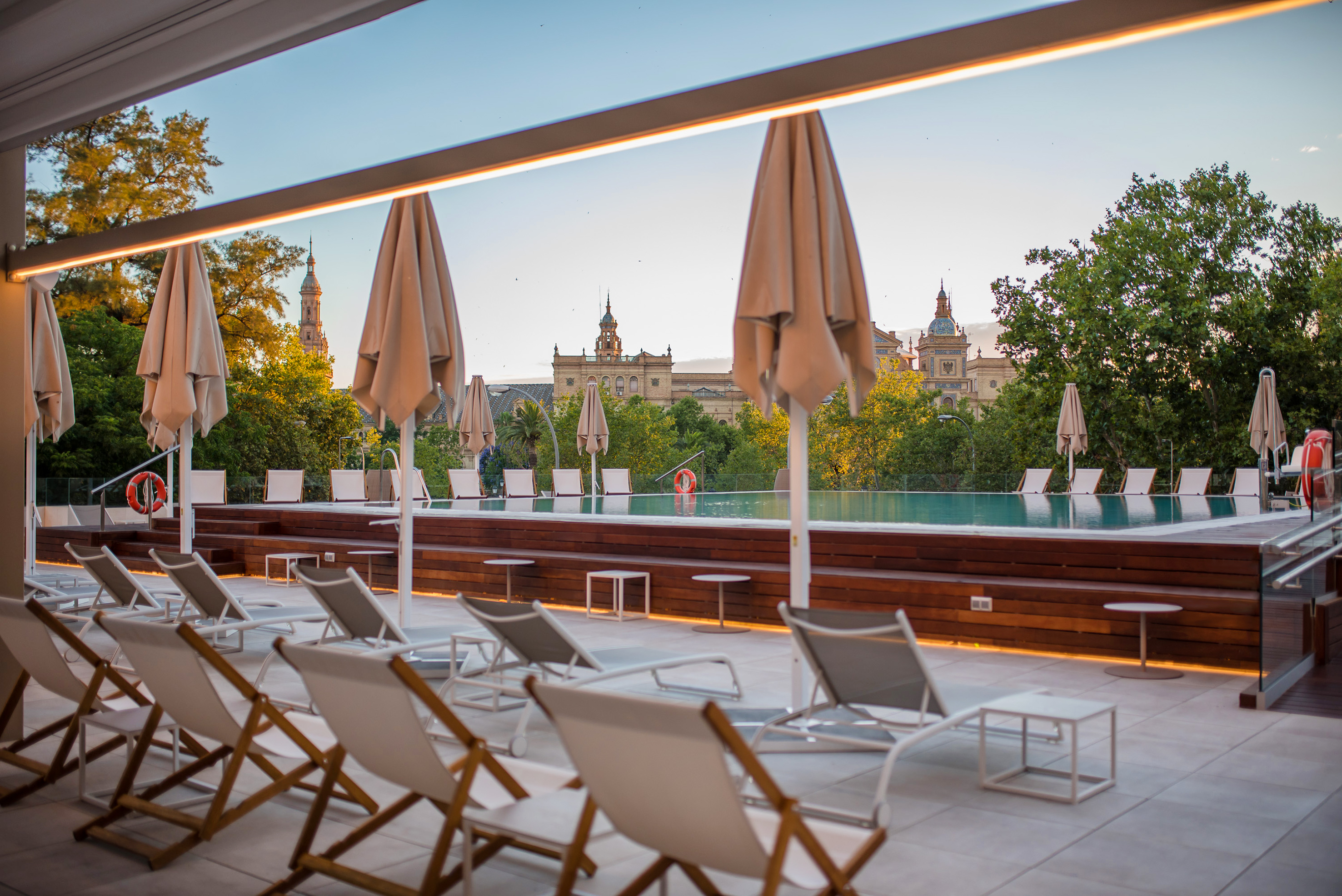 Rooftop infinity pool with lounge chairs, umbrellas, and historic Seville cityscape.