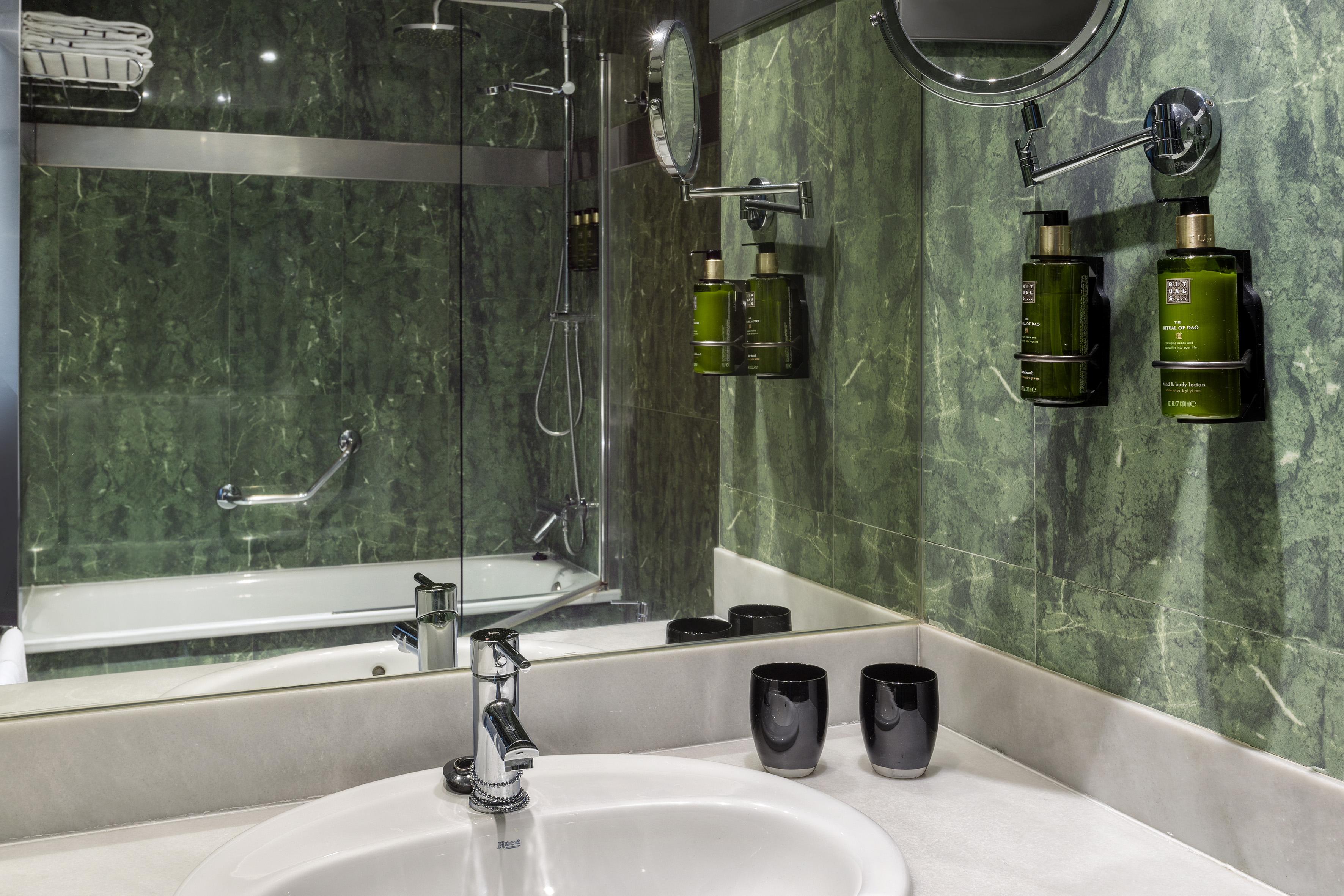 Green marble bathroom with sink, mirror, shower, and Rituals products.