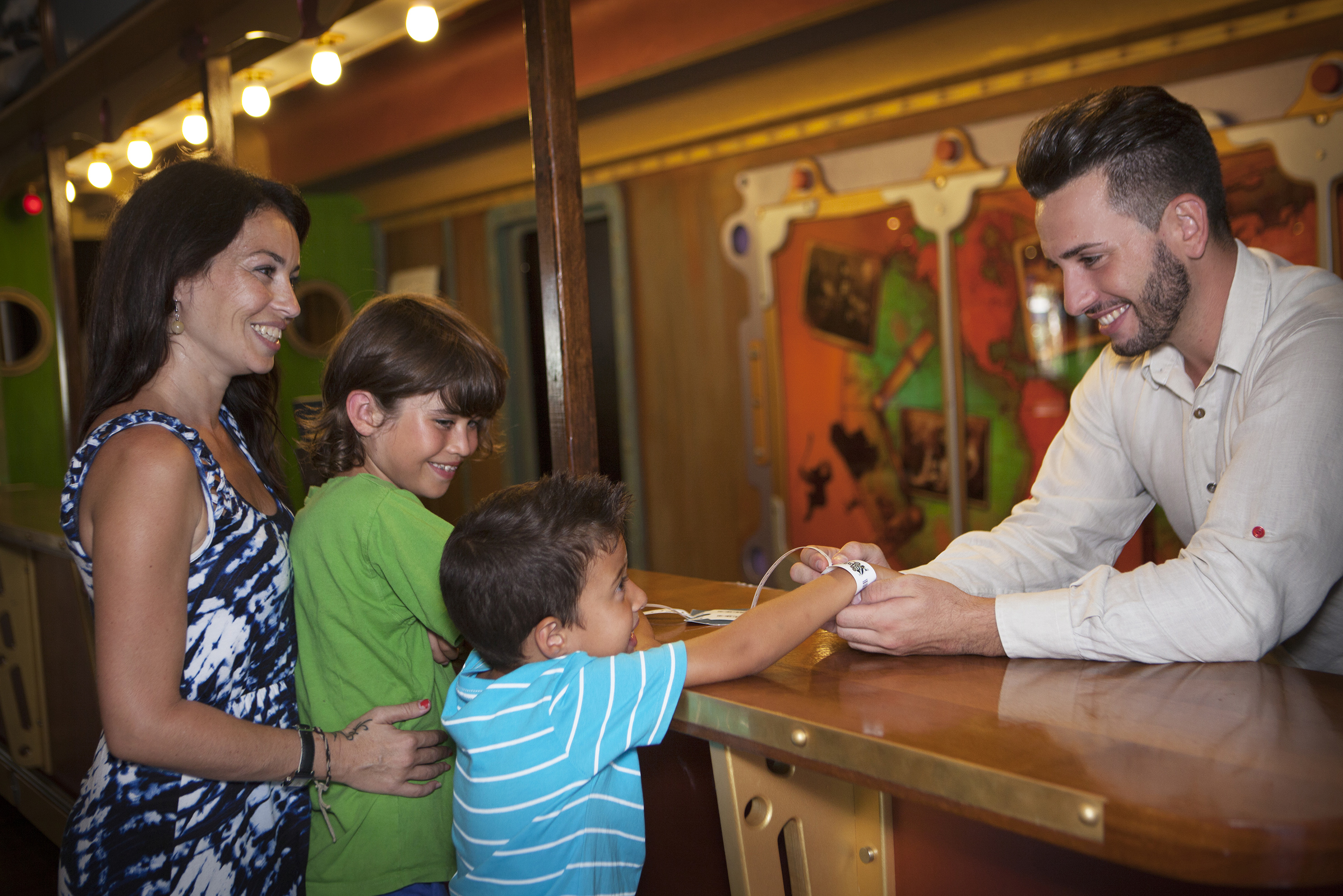 Family with two boys getting entry wristbands from attendant, all smiling.