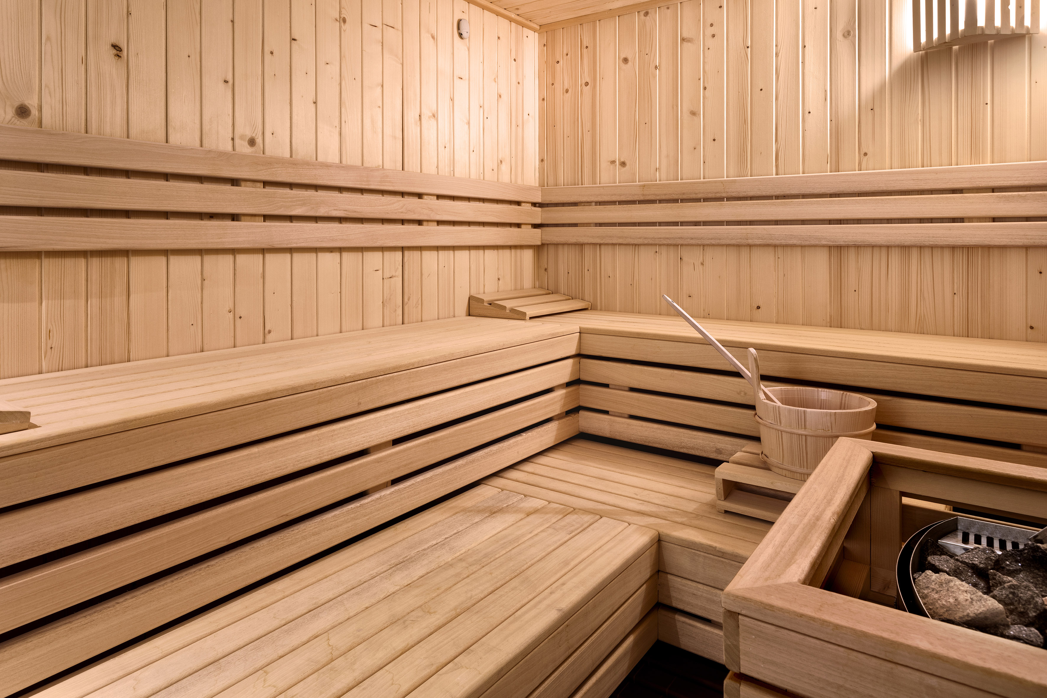 Empty traditional wooden sauna with benches, heater, bucket, and ladle.