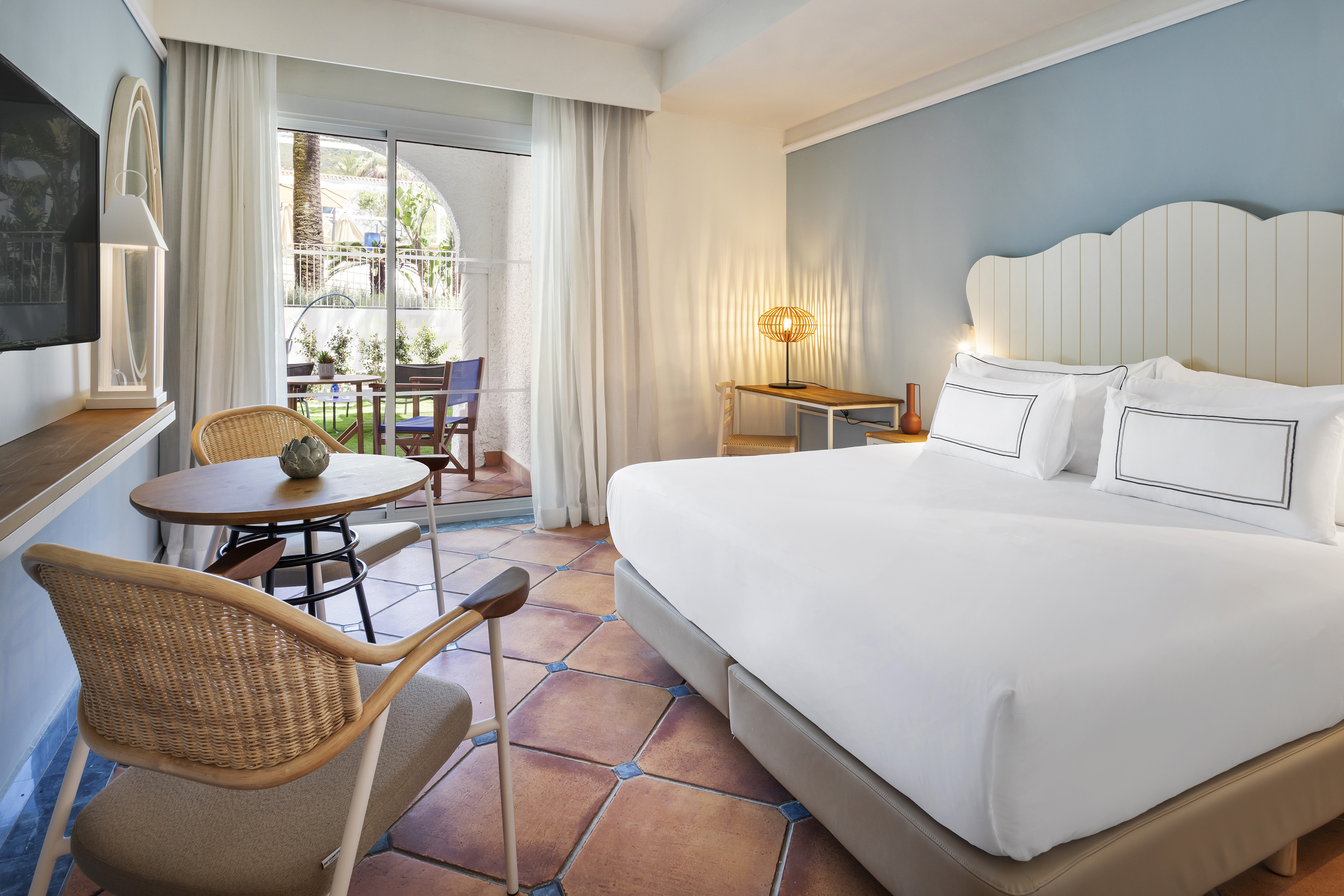 Modern hotel room with large bed, terracotta floor, and balcony access.