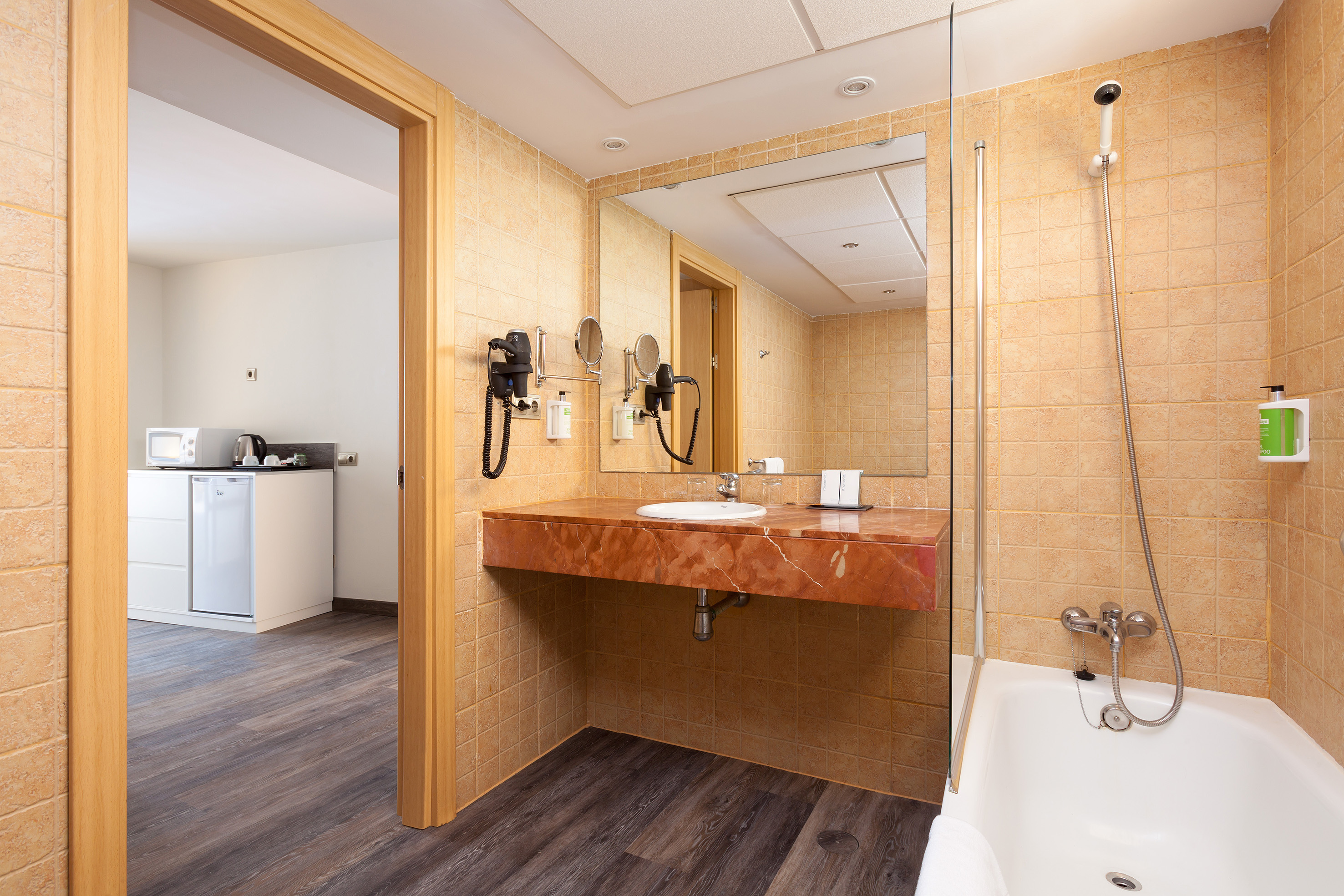 Hotel bathroom with vanity, sink, tiled walls, bathtub, and kitchenette view.