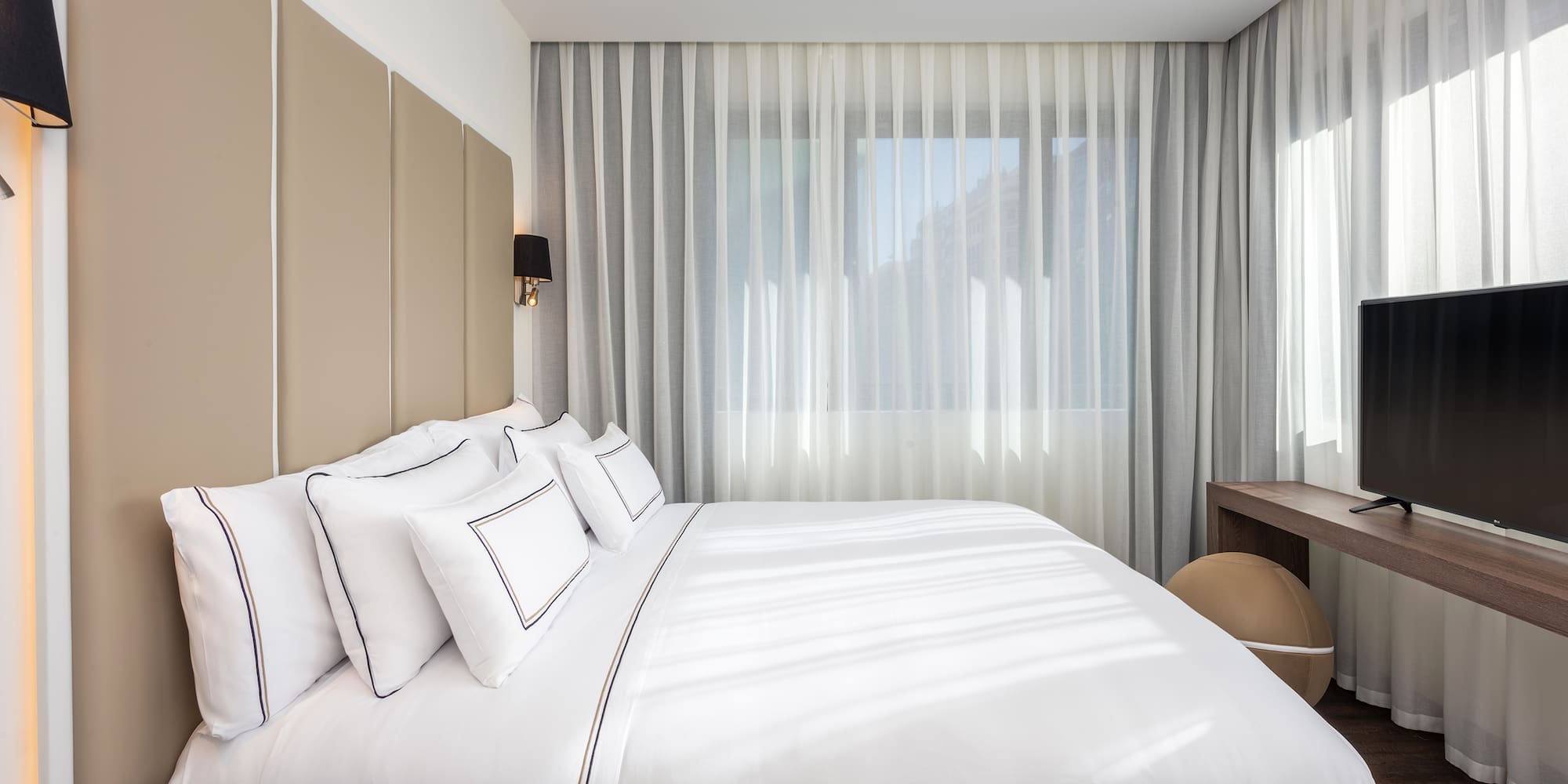 a bed with white sheets and a desk in a room with curtains