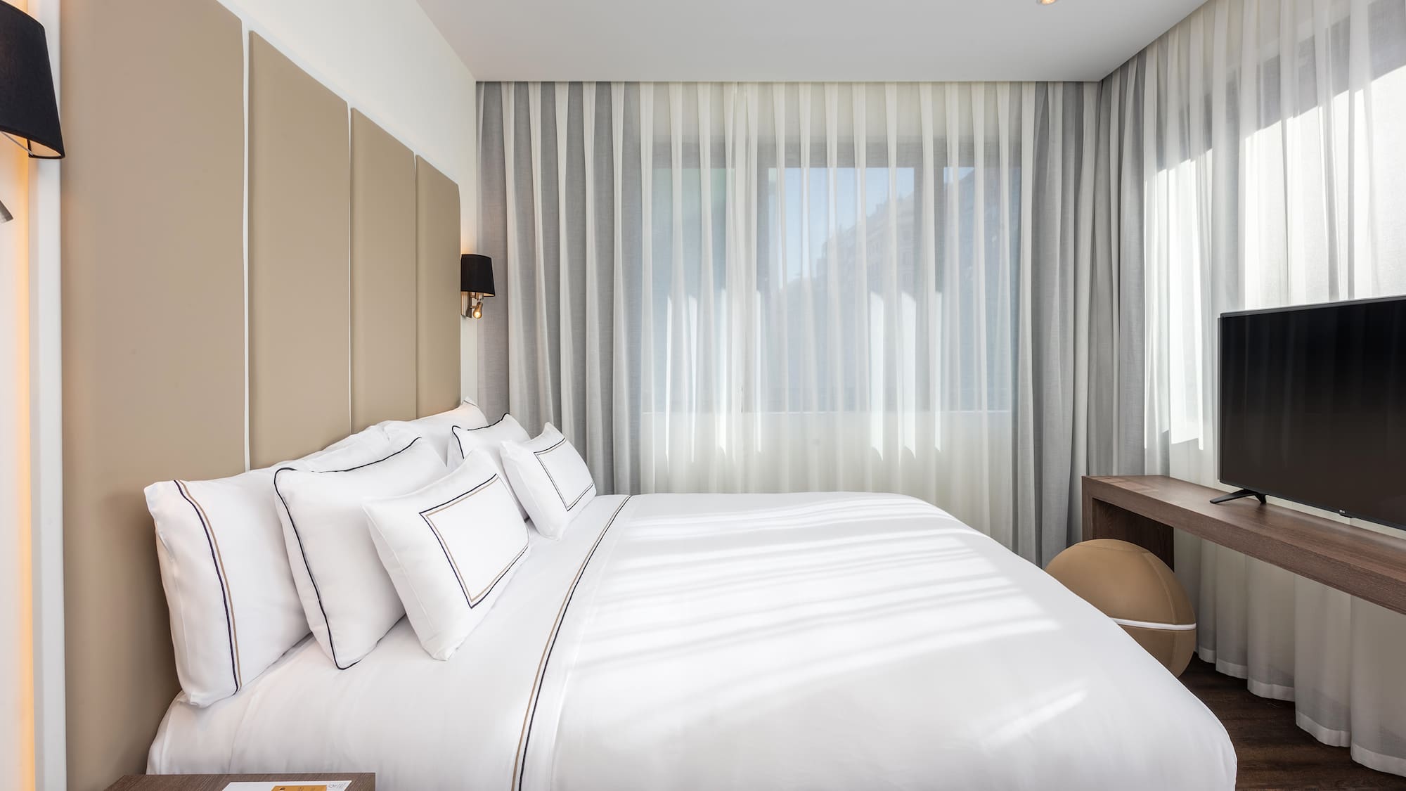 a bed with white sheets and a desk in a room with curtains