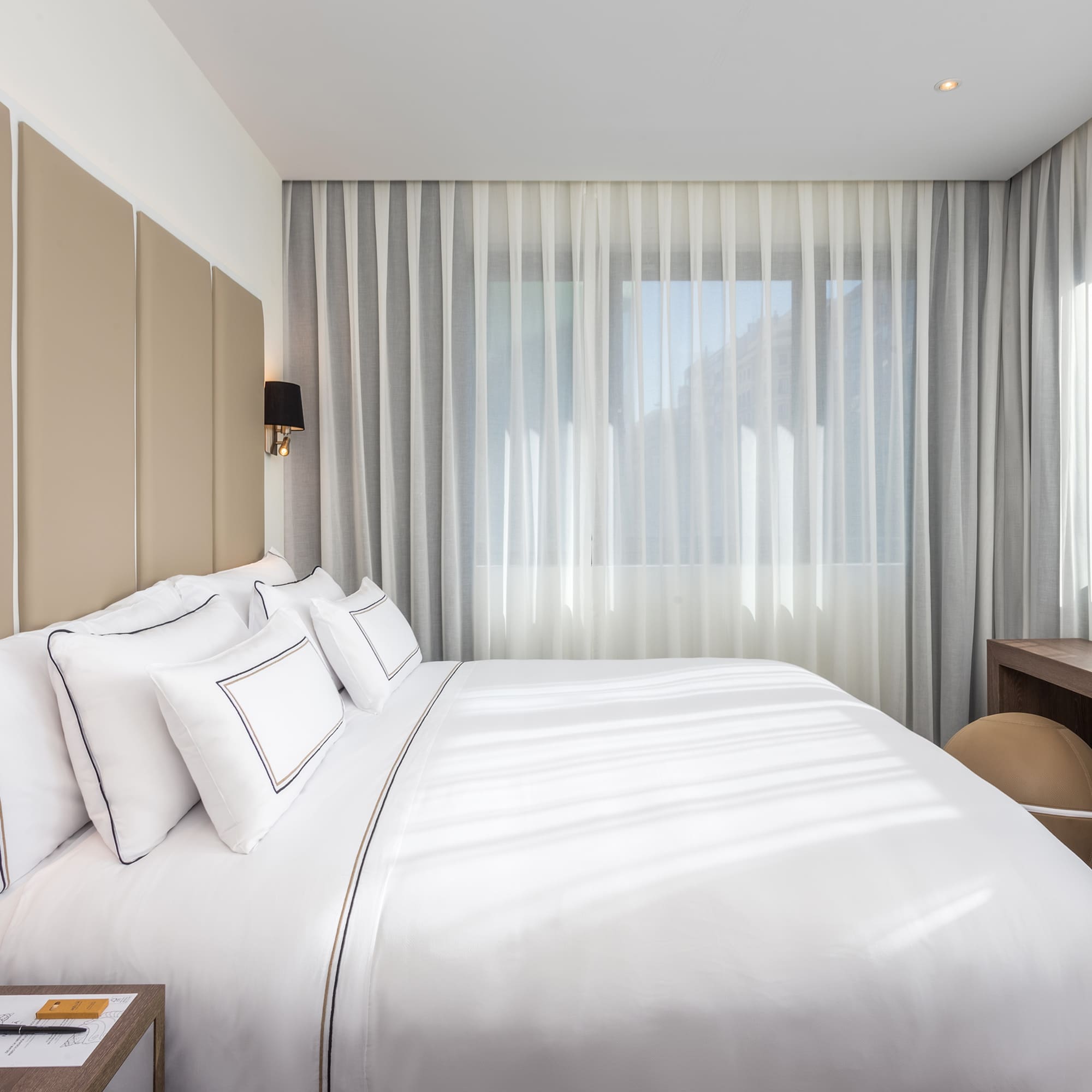 a bed with white sheets and a desk in a room with curtains