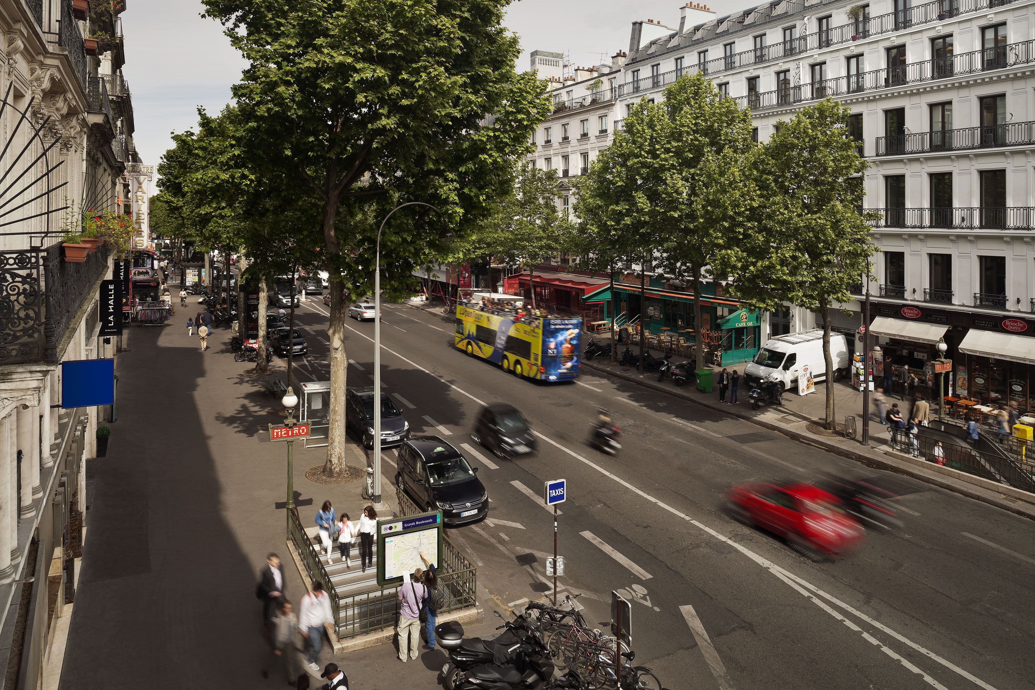 Paris street with Metro entrance, double-decker tour bus, blurred traffic, and people.