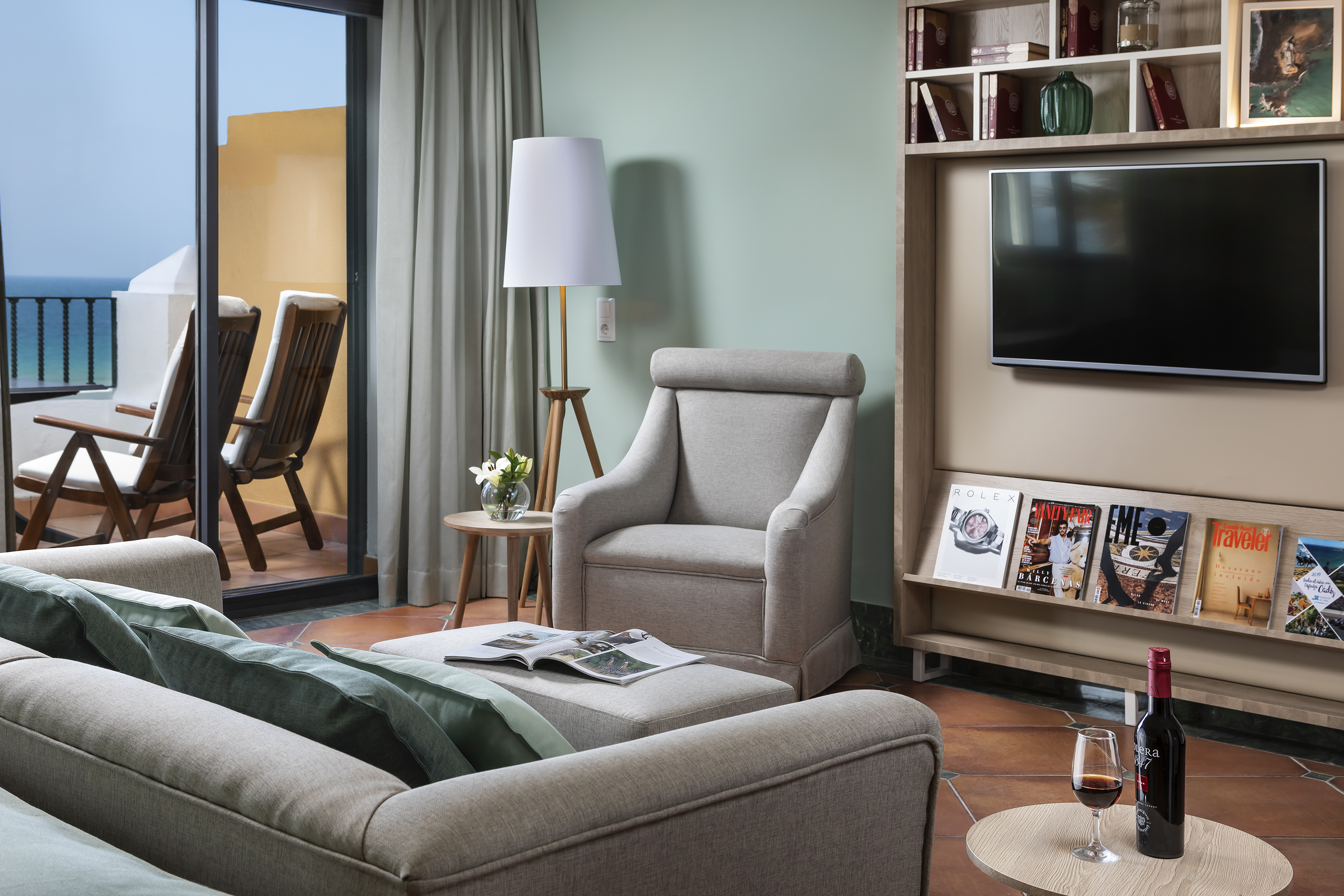Modern hotel living room with ocean view balcony, sofa, armchair, and TV.