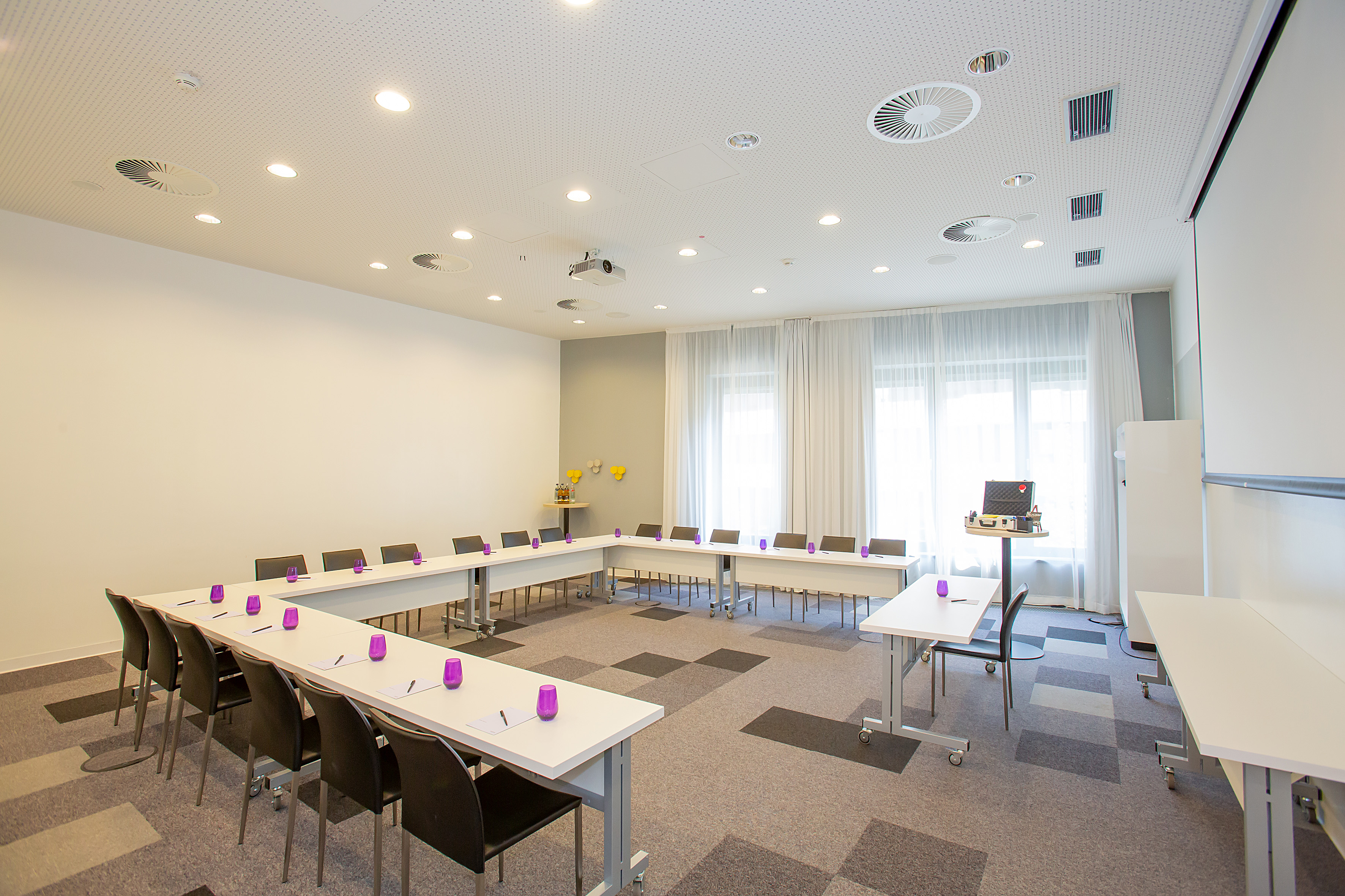 Modern U-shape conference room with projector, screen, and bright lighting.