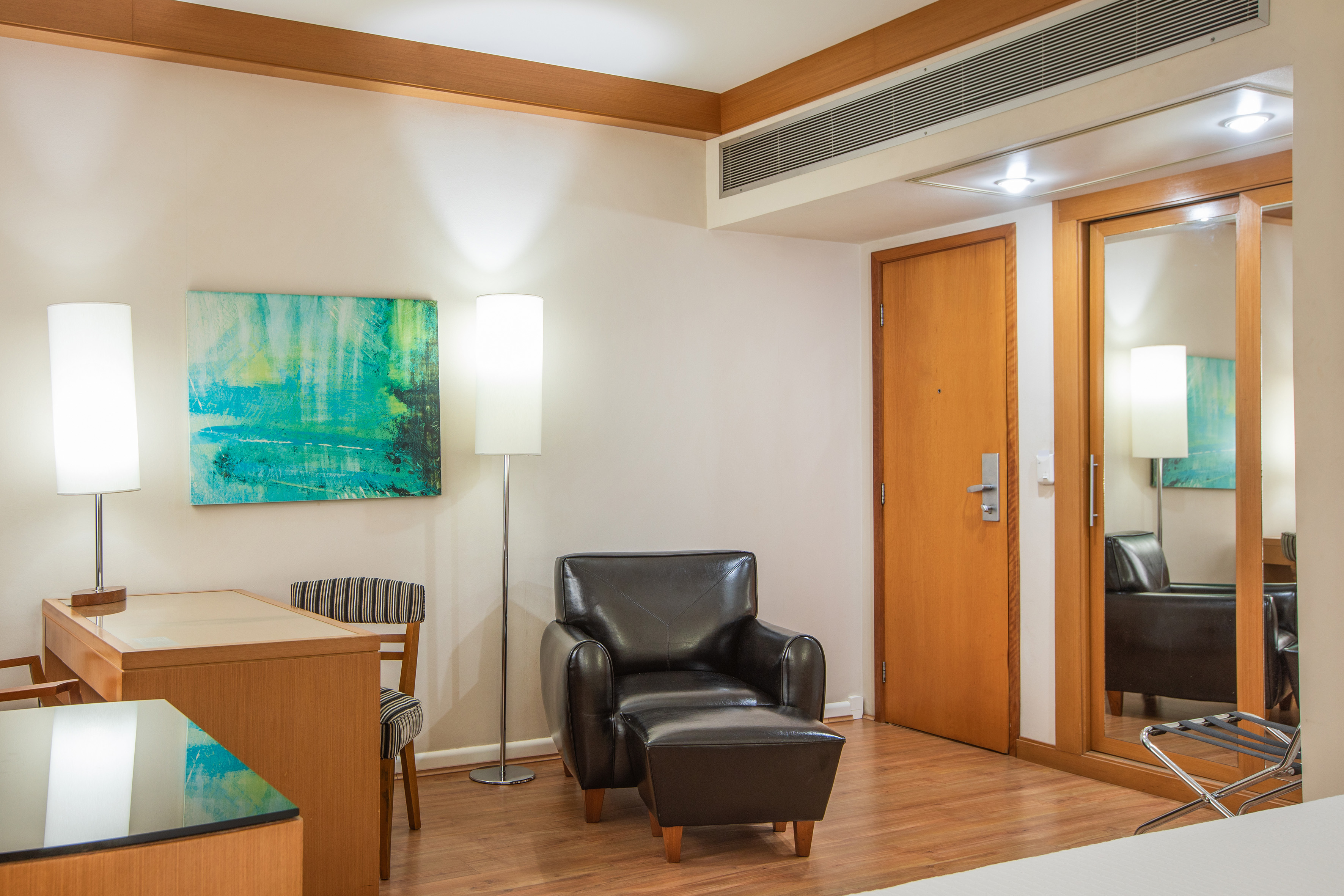Hotel room with desk, chair, leather armchair, floor lamps, and abstract art.