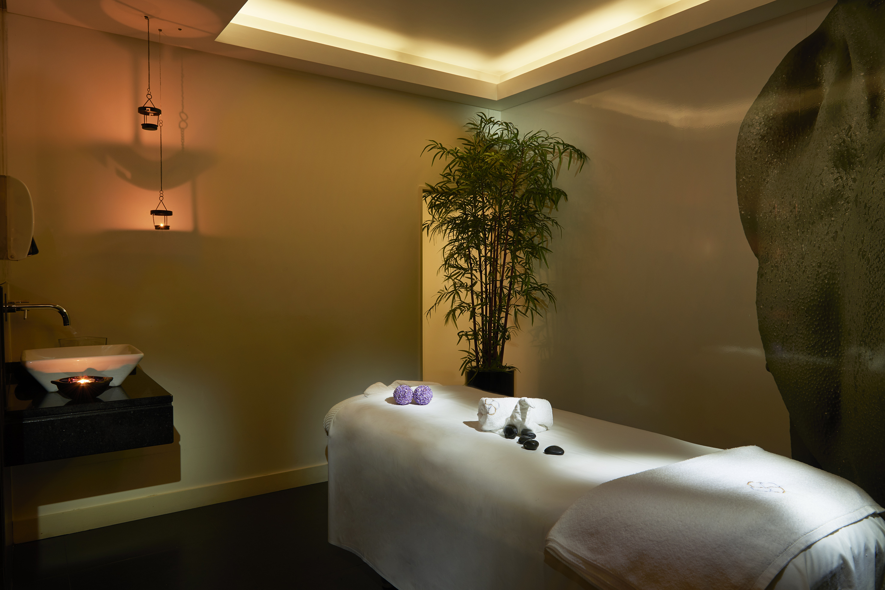 Relaxing spa room with massage table, hot stones, towels, and warm ambient lighting.