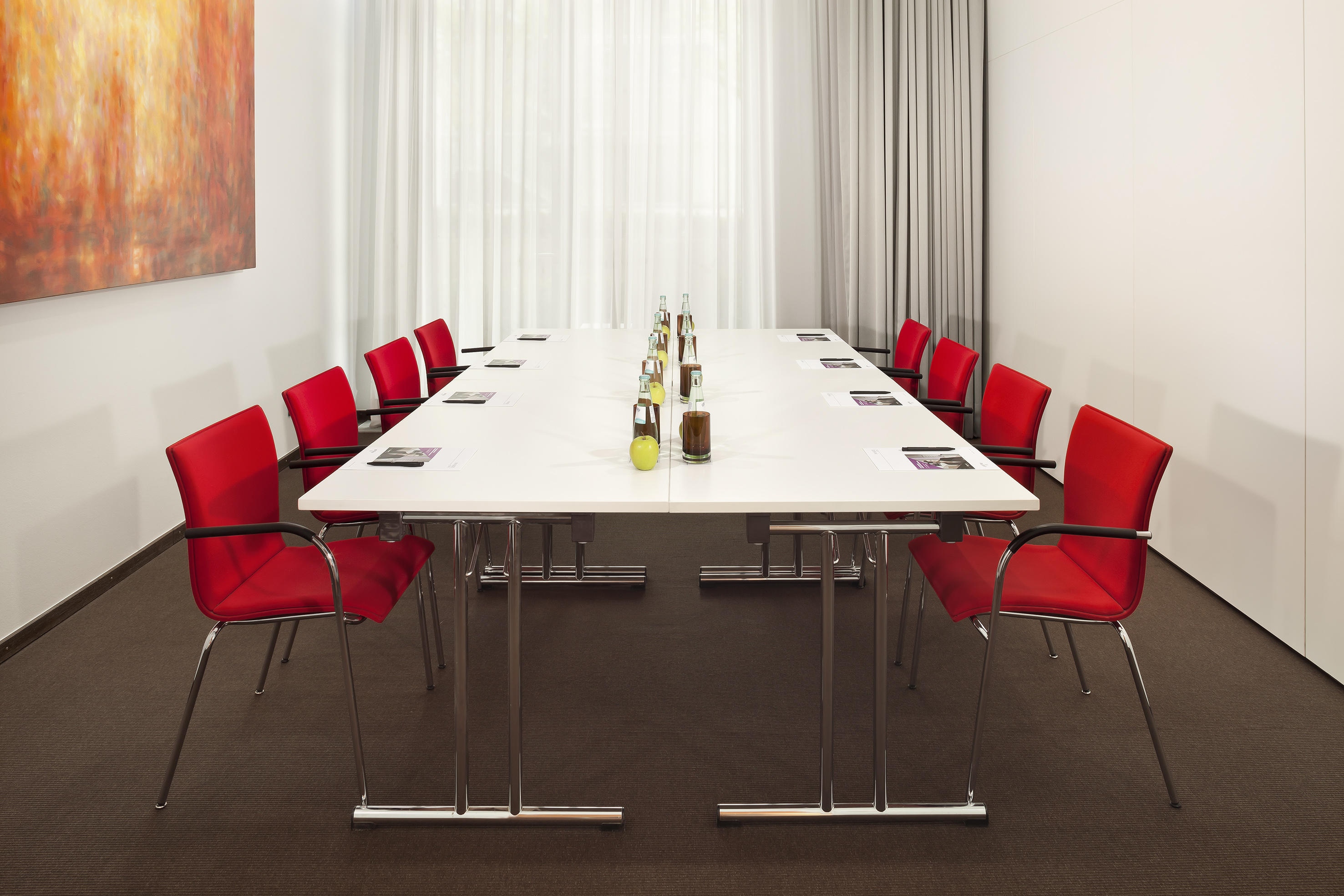 Contemporary meeting room with white table, bright red chairs, and abstract art.