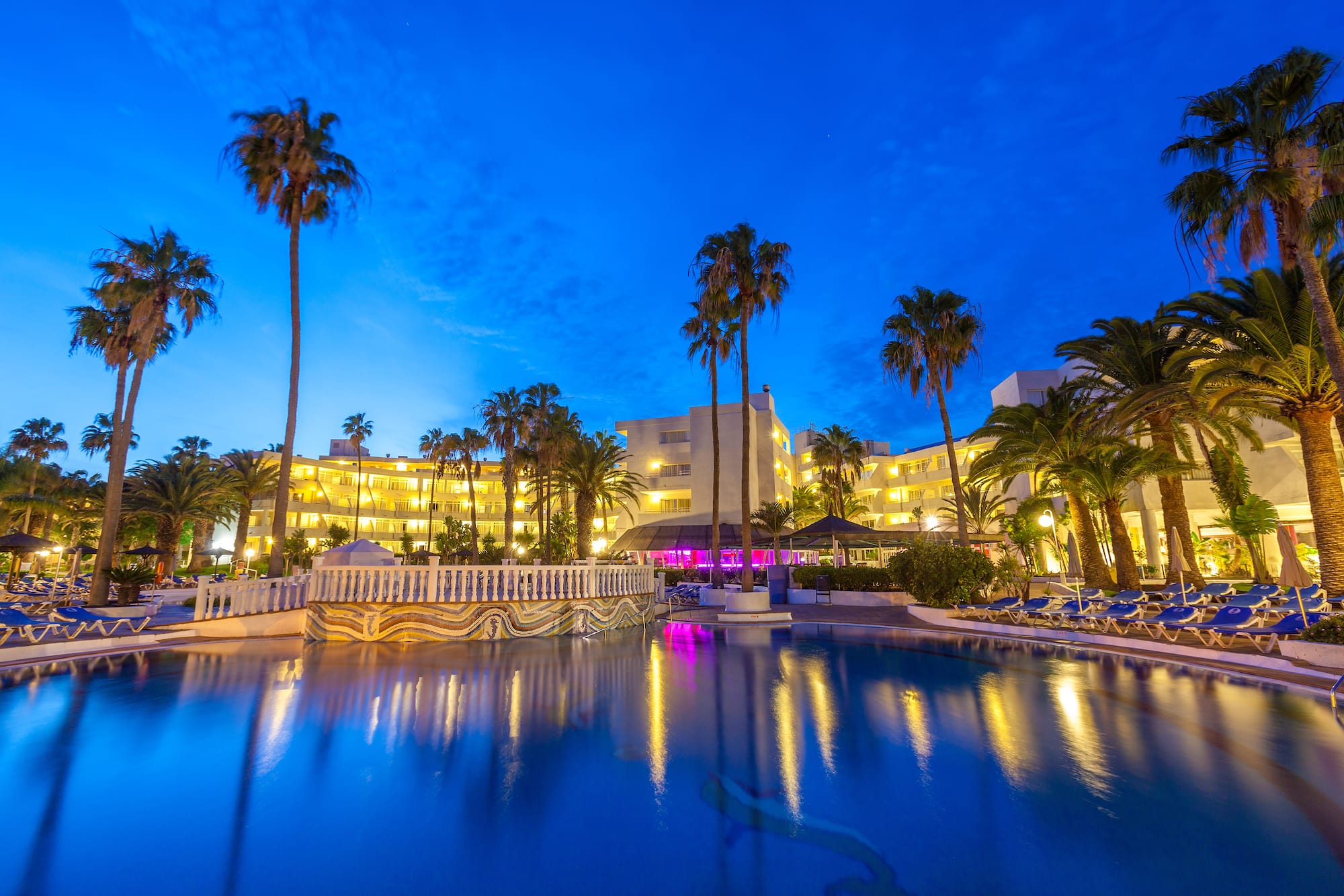 a pool with palm trees and buildings in the background