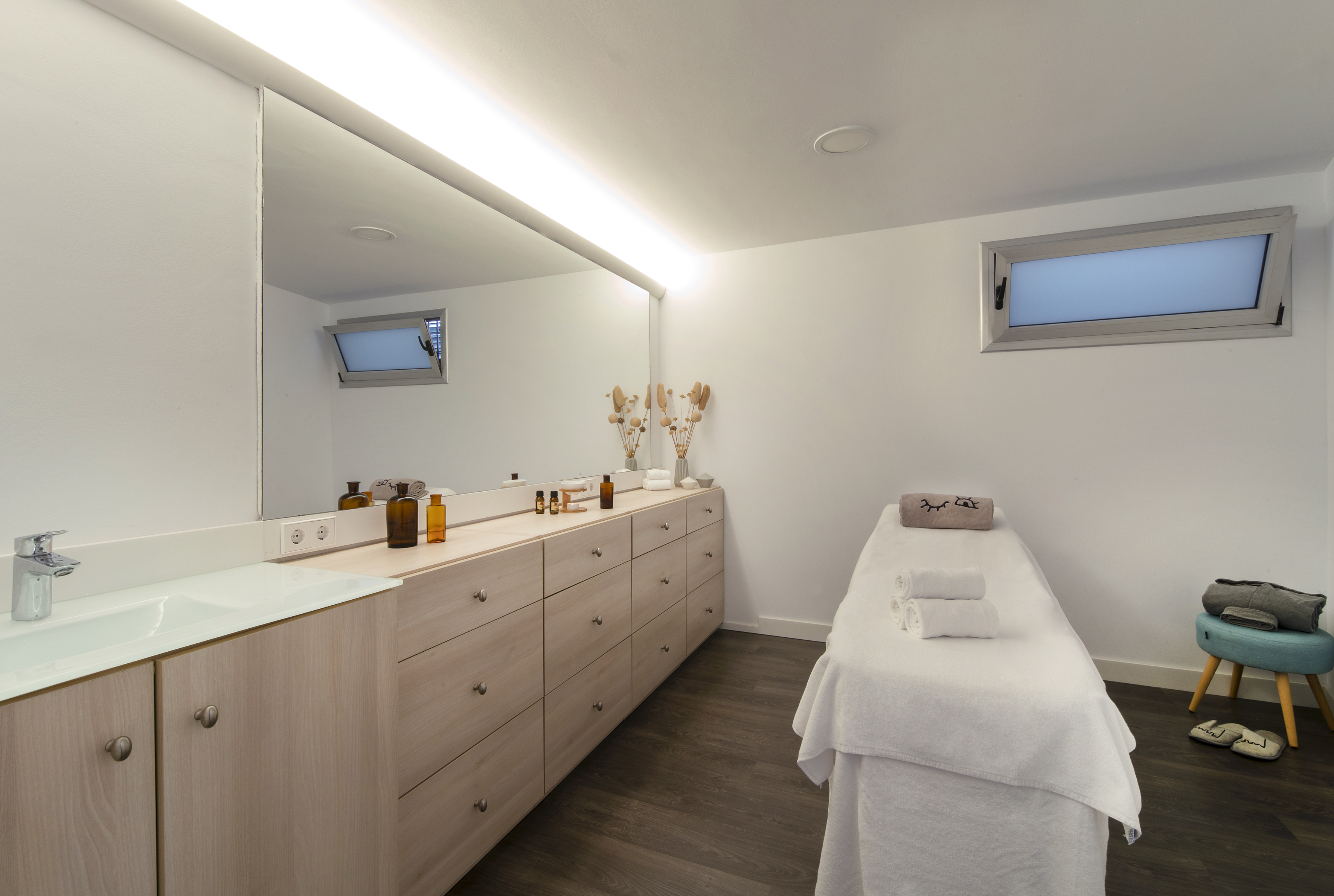Clean modern wellness spa room with massage table, wooden vanity, and large mirror.