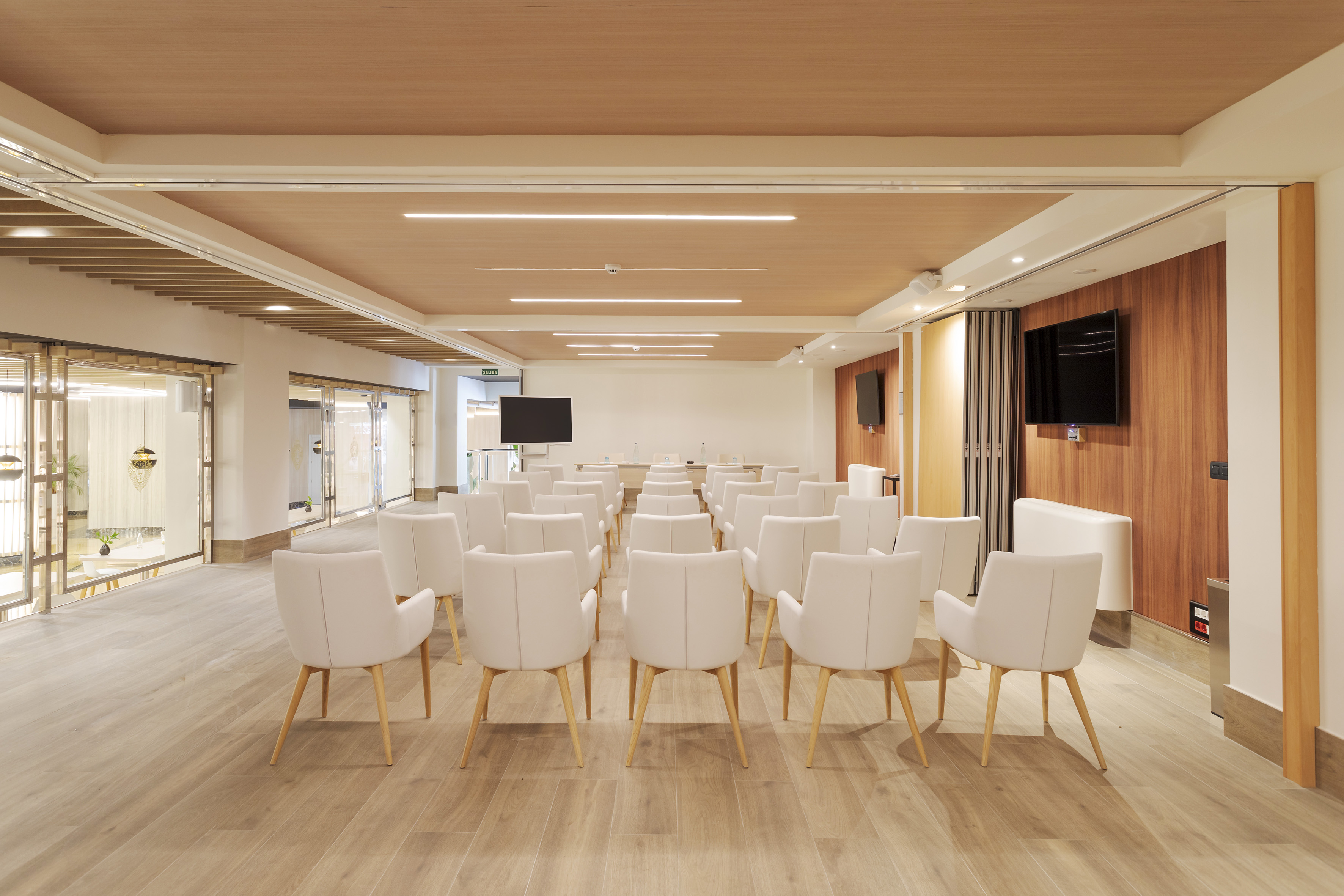 Modern conference room with white chairs, wooden floor, and presentation screens.