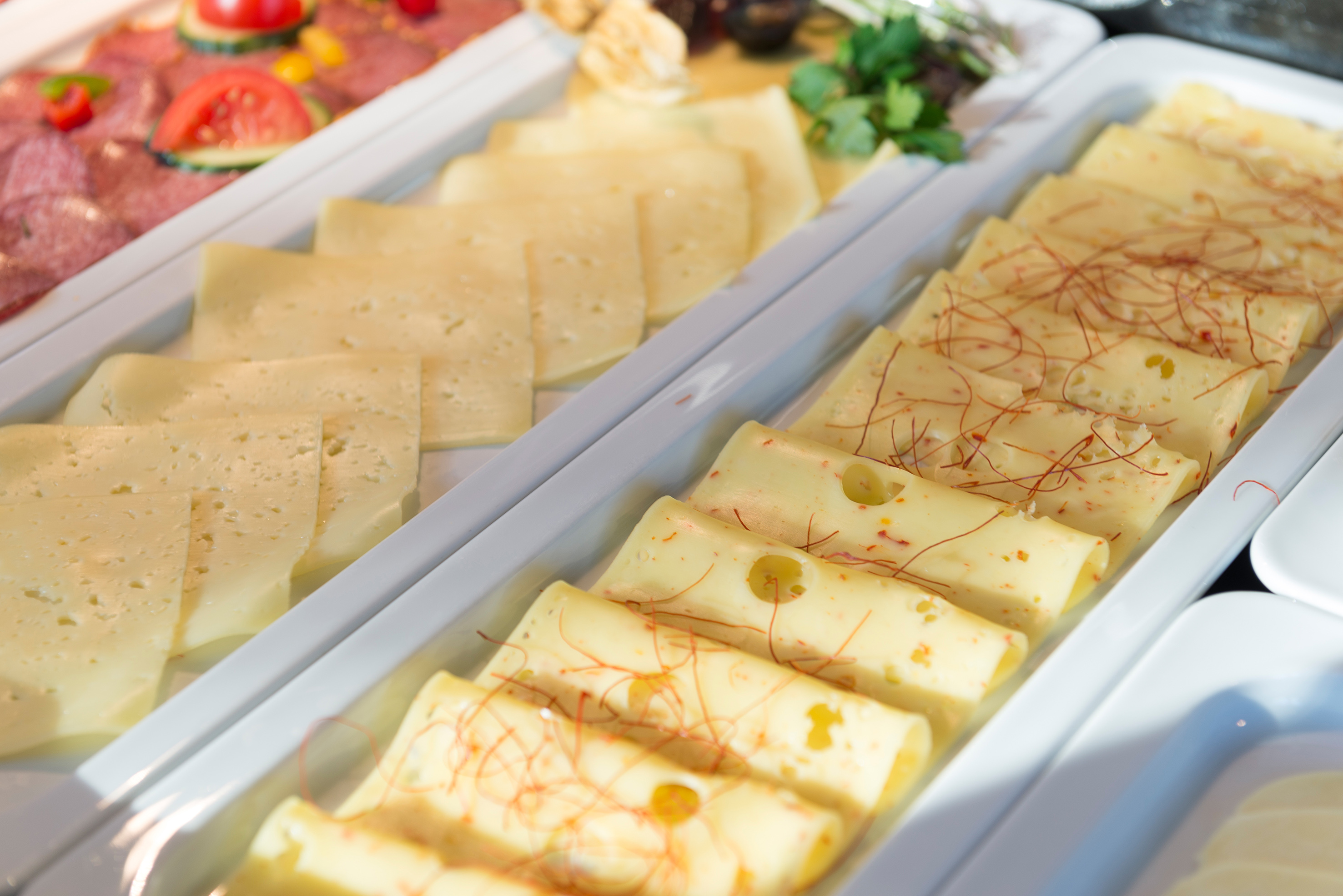 Buffet spread with plain and spiced sliced cheese, some rolled, beside cold cuts.