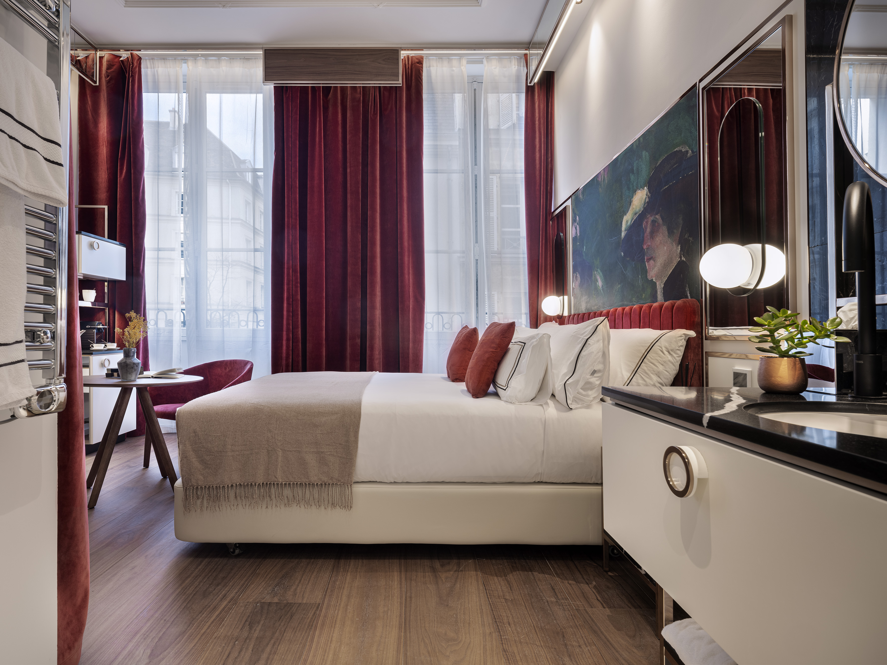 Chic hotel bedroom: white bed, red velvet curtains, large artwork, sleek vanity.