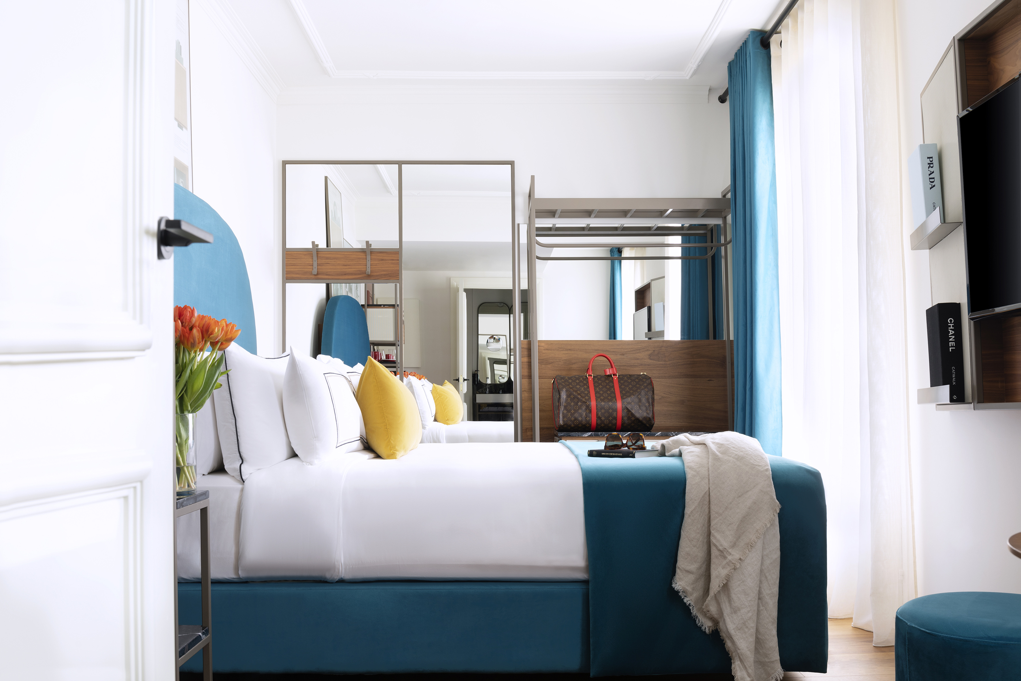 Modern luxury hotel room with blue bed, Louis Vuitton bag, and designer books.