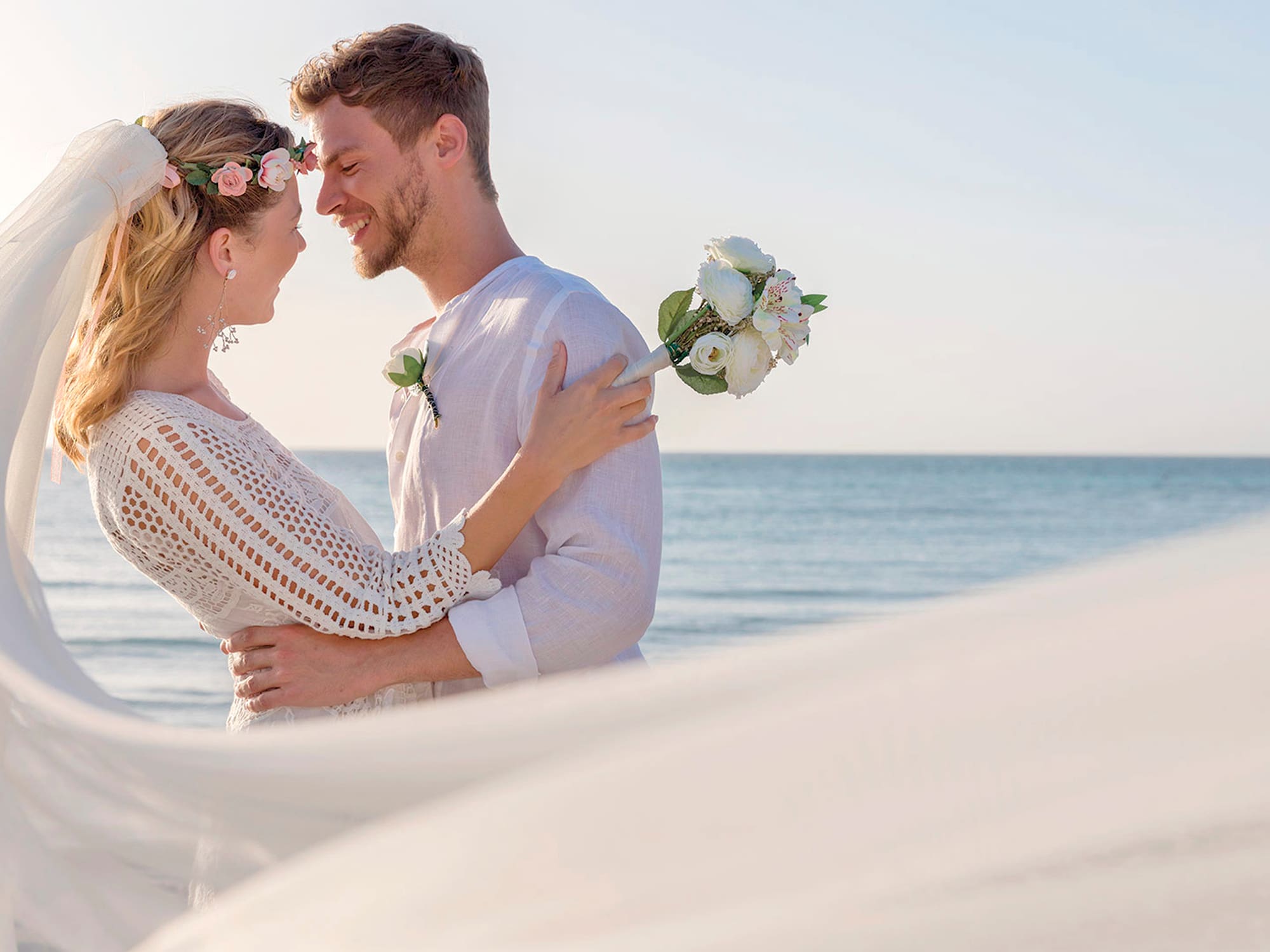 a man and woman holding flowers and standing on a beach