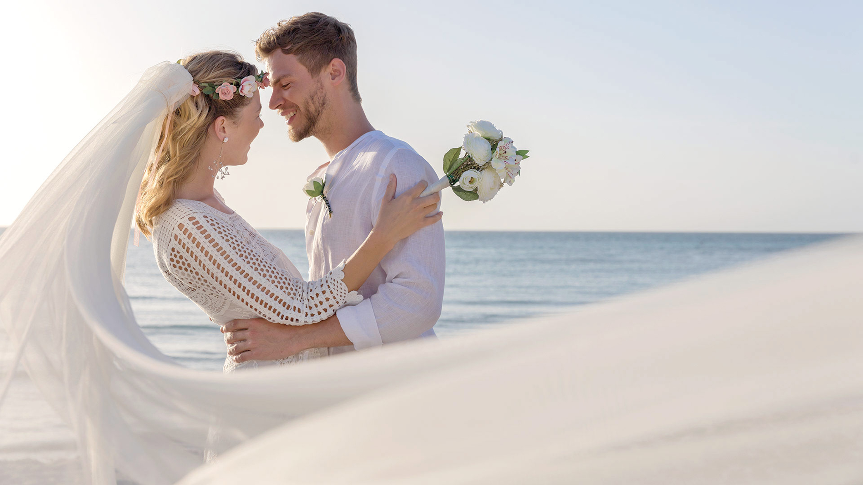 a man and woman holding flowers and standing on a beach