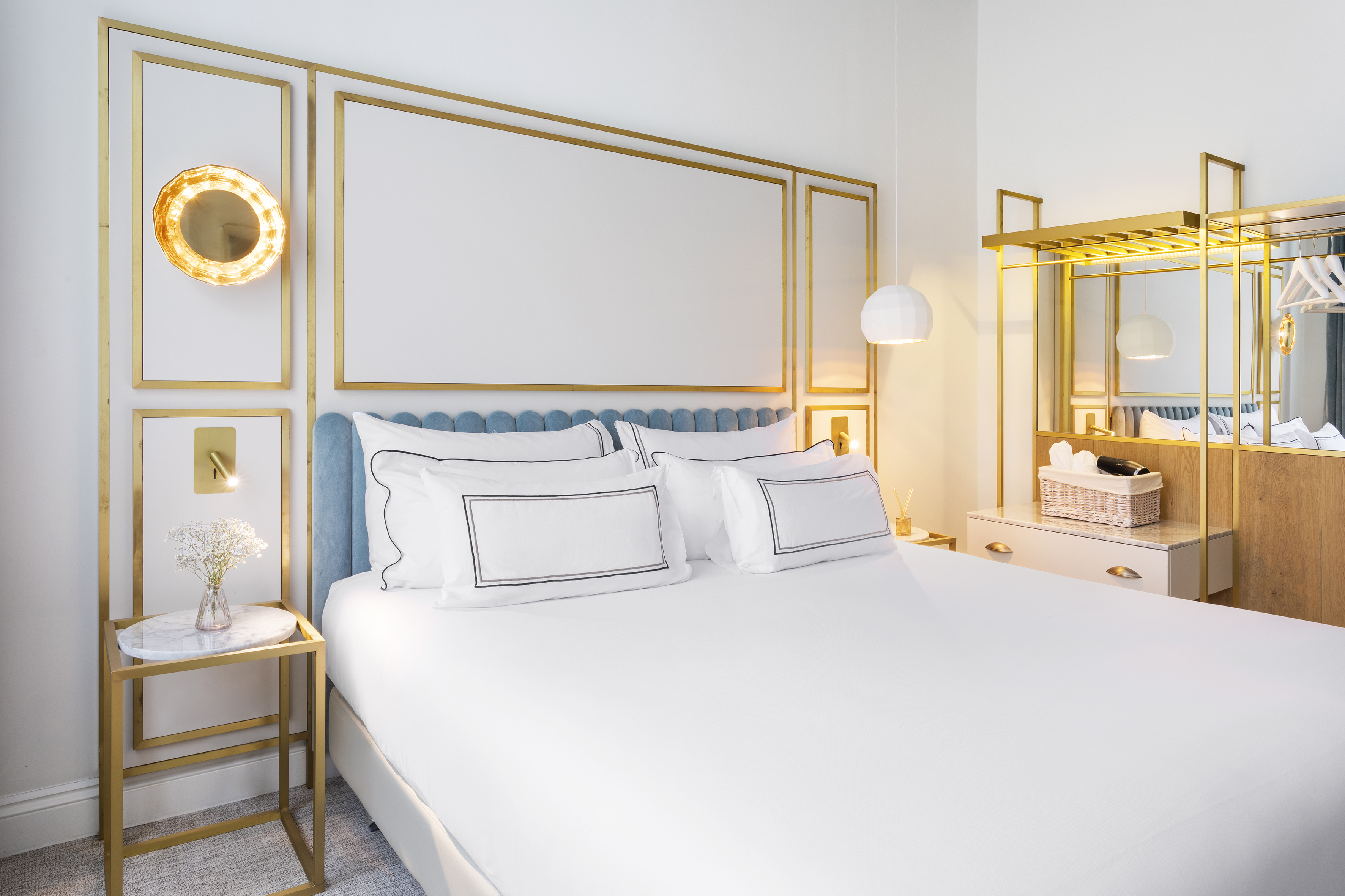Hotel bedroom featuring white bed, blue scalloped headboard, and gold wall decor.