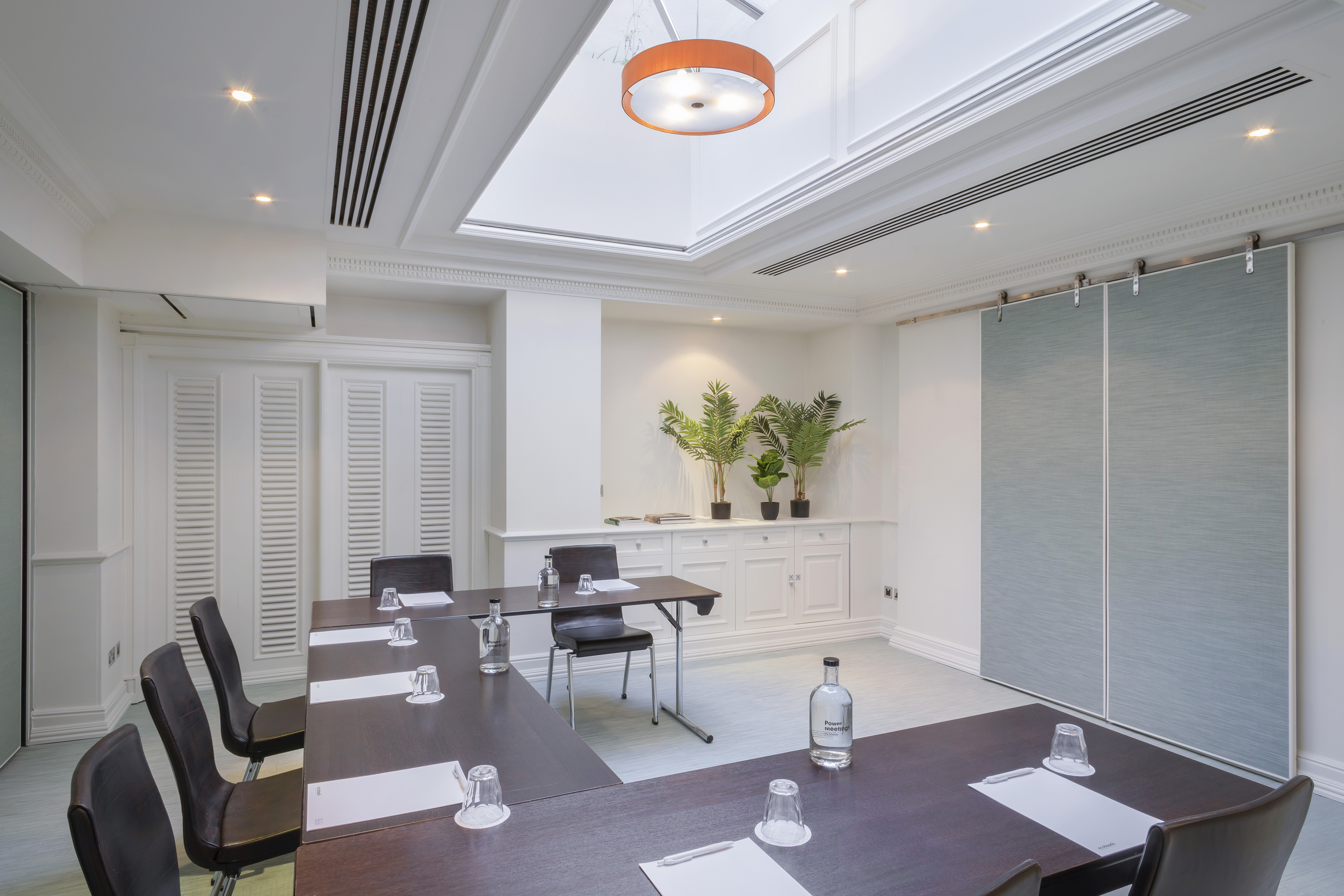 Elegant boardroom with U-shaped table, bright skylight, and modern sliding panels.