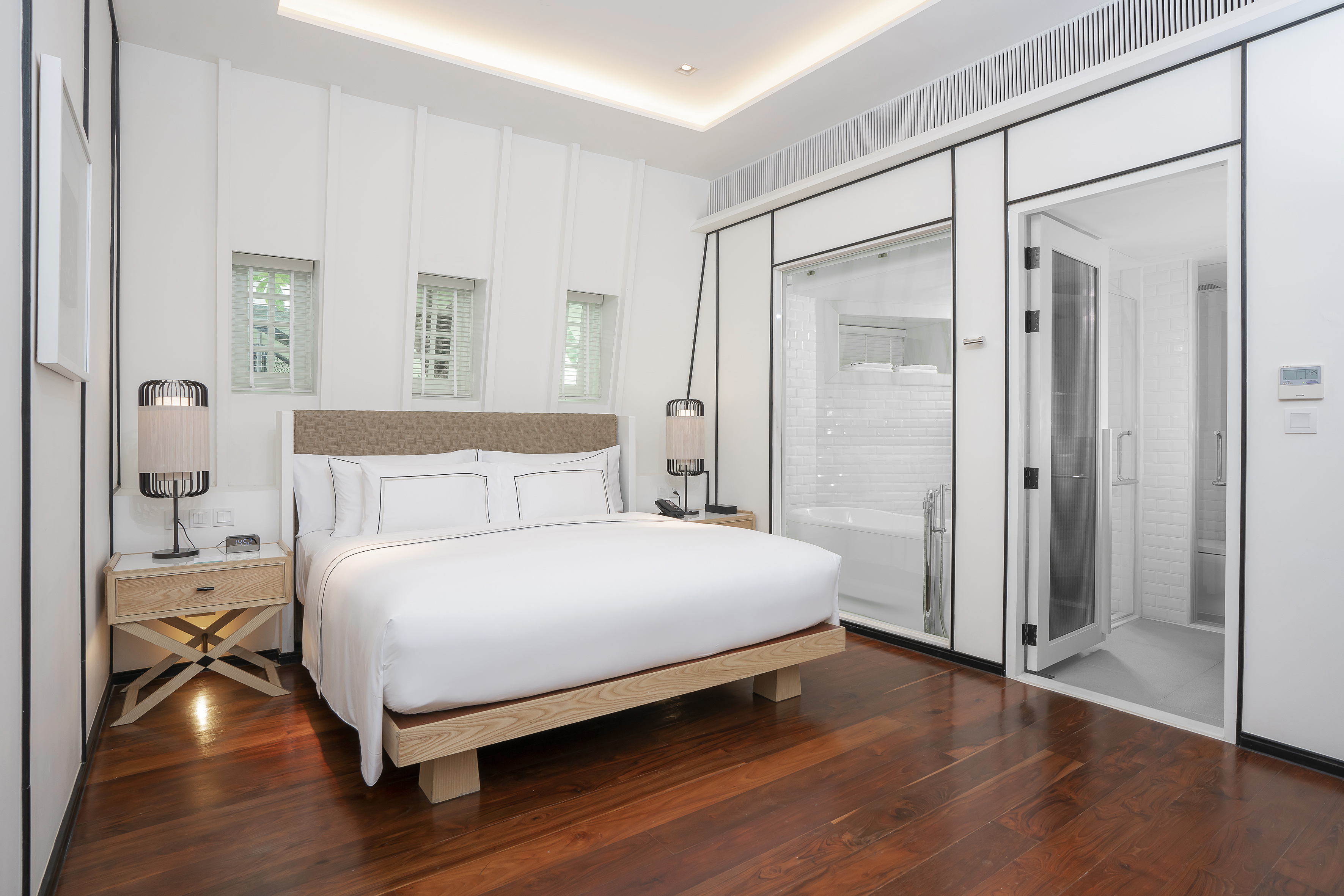 Modern white bedroom with wood floor, king bed, and glass-enclosed bathroom.