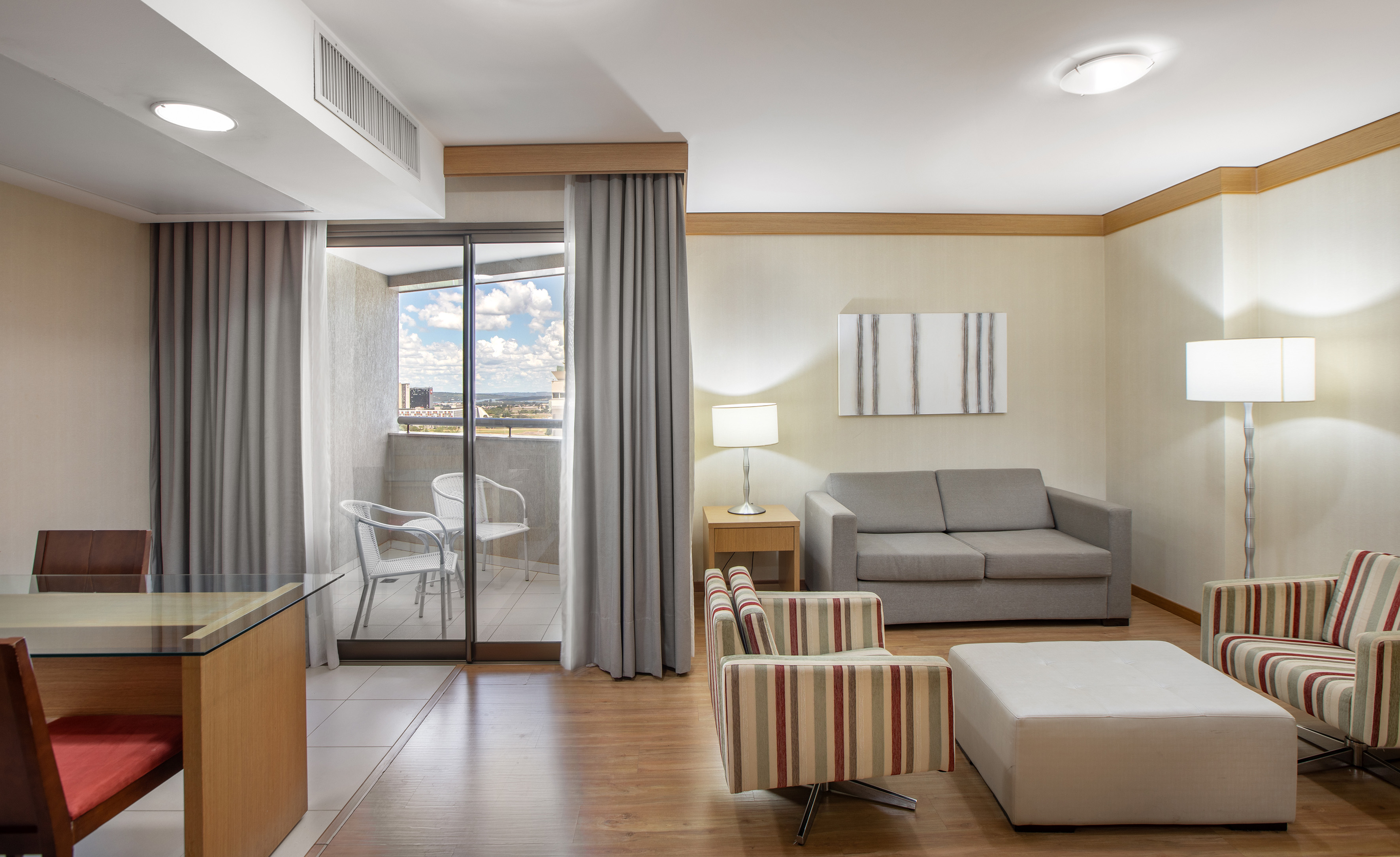 Modern hotel suite living room with balcony city view and dining area.