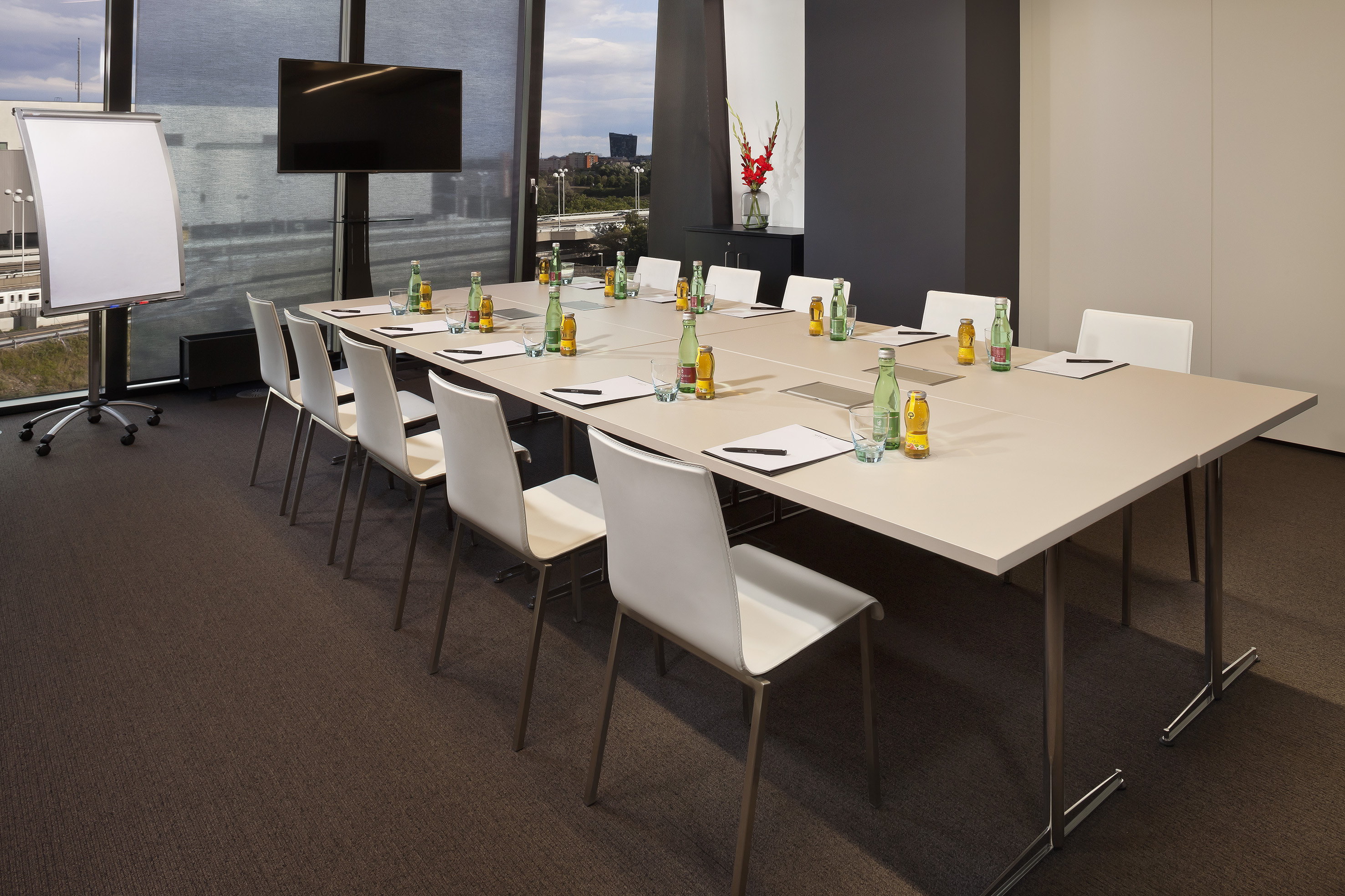 Modern conference room with long table, white chairs, flip chart, and monitor.