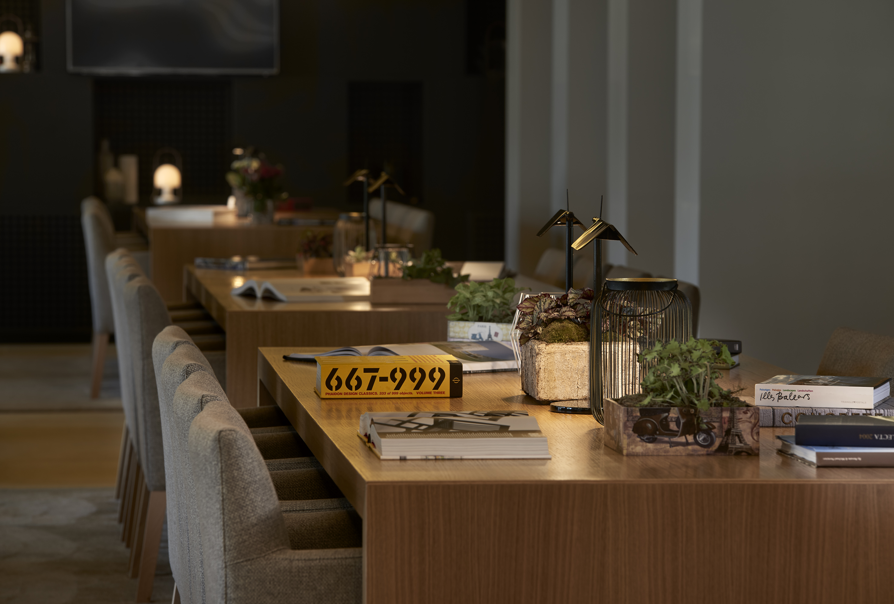 Elegant hotel lounge table with chairs, decorative books, and potted greenery.