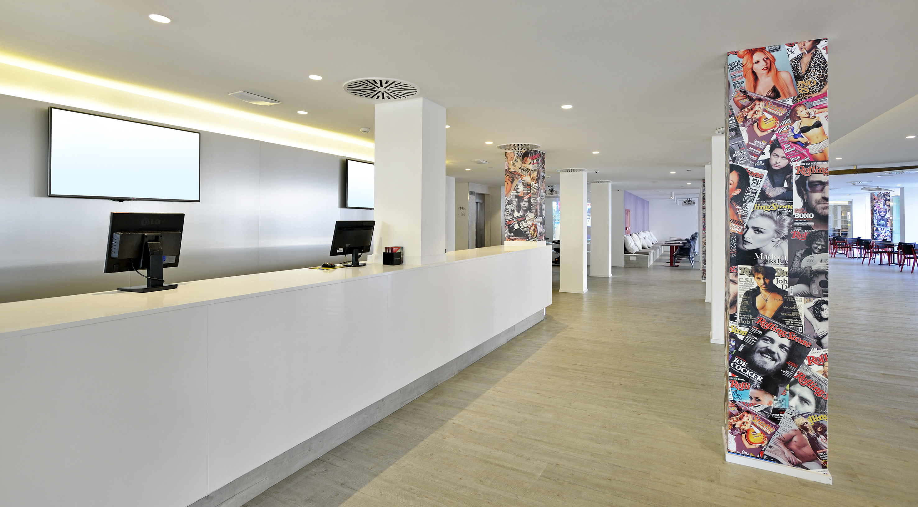 Modern hotel reception and lobby with digital screens, magazine-wrapped pillars.