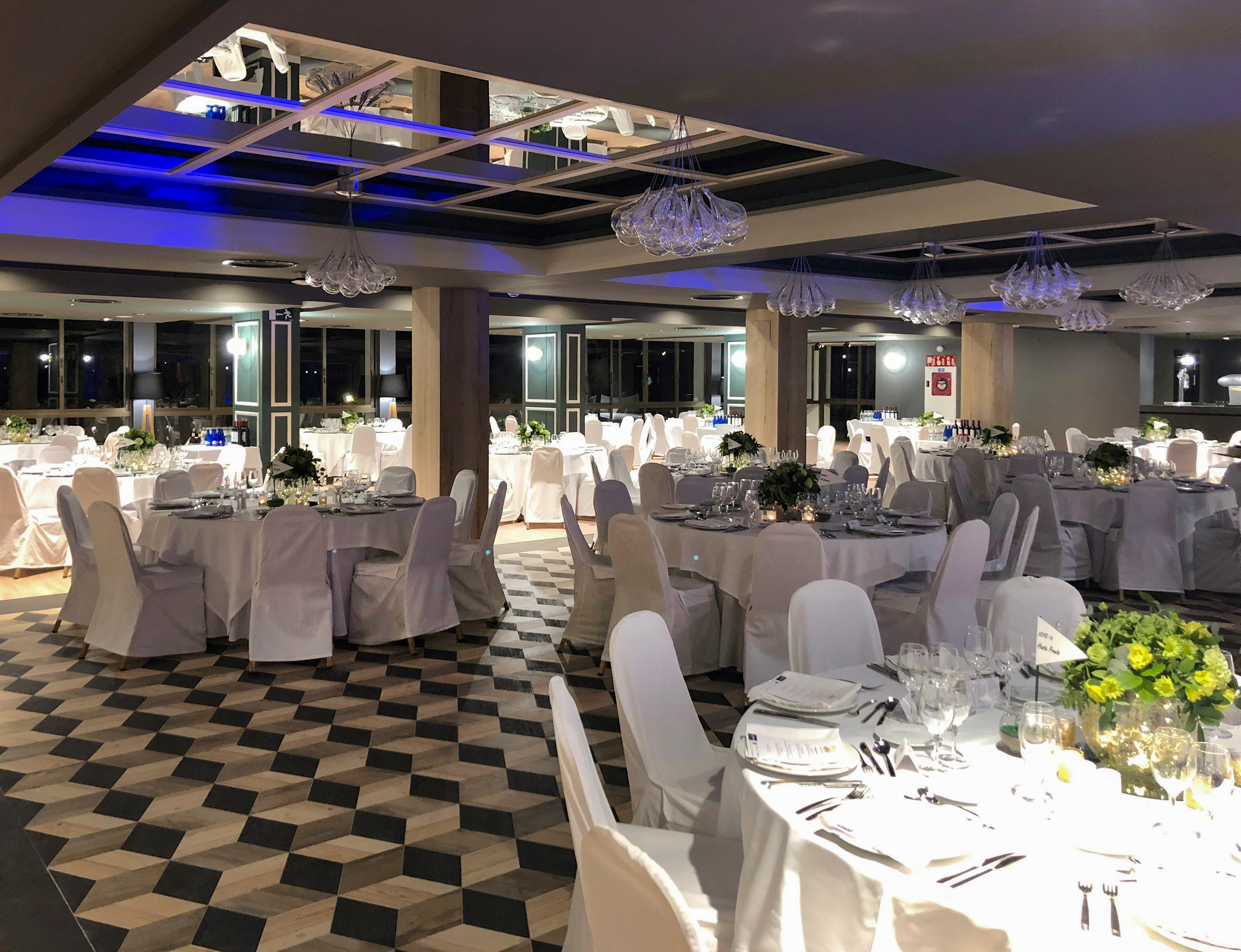Elegant event hall with white tables, modern chandeliers, and geometric floor.