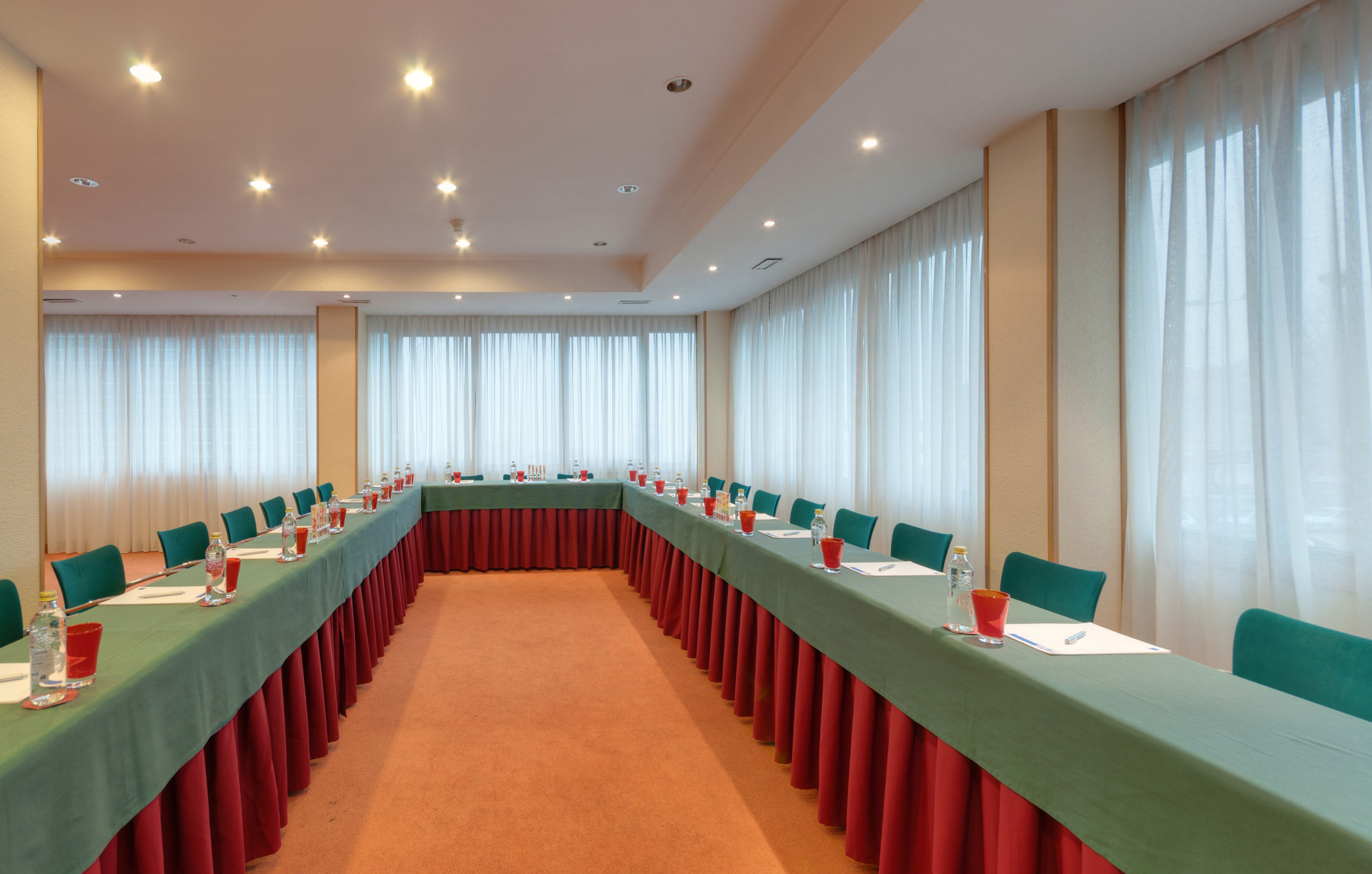 U-shape meeting room setup with green tables, teal chairs, and white curtains.