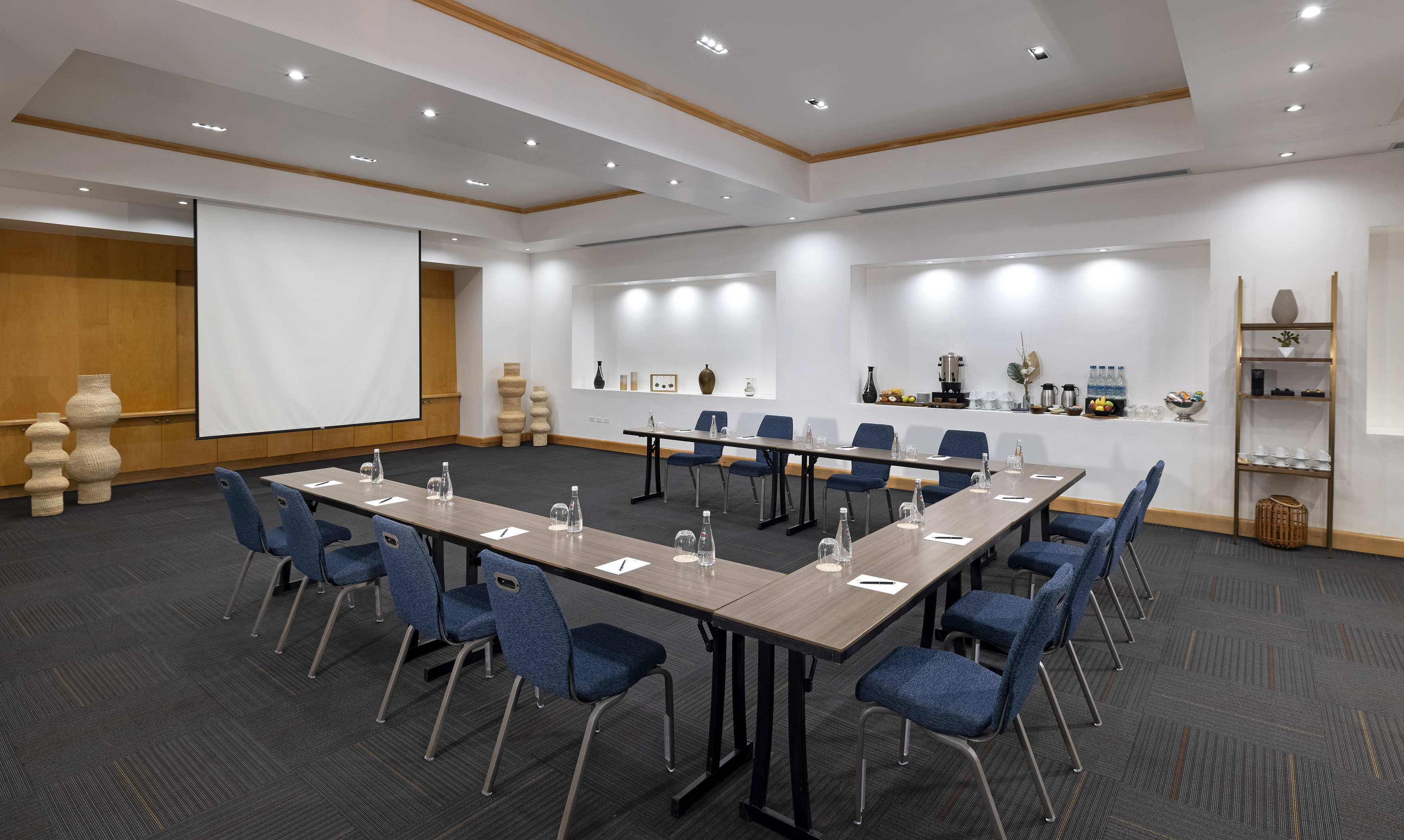 U-shape meeting room with projector screen, blue chairs, and refreshments.